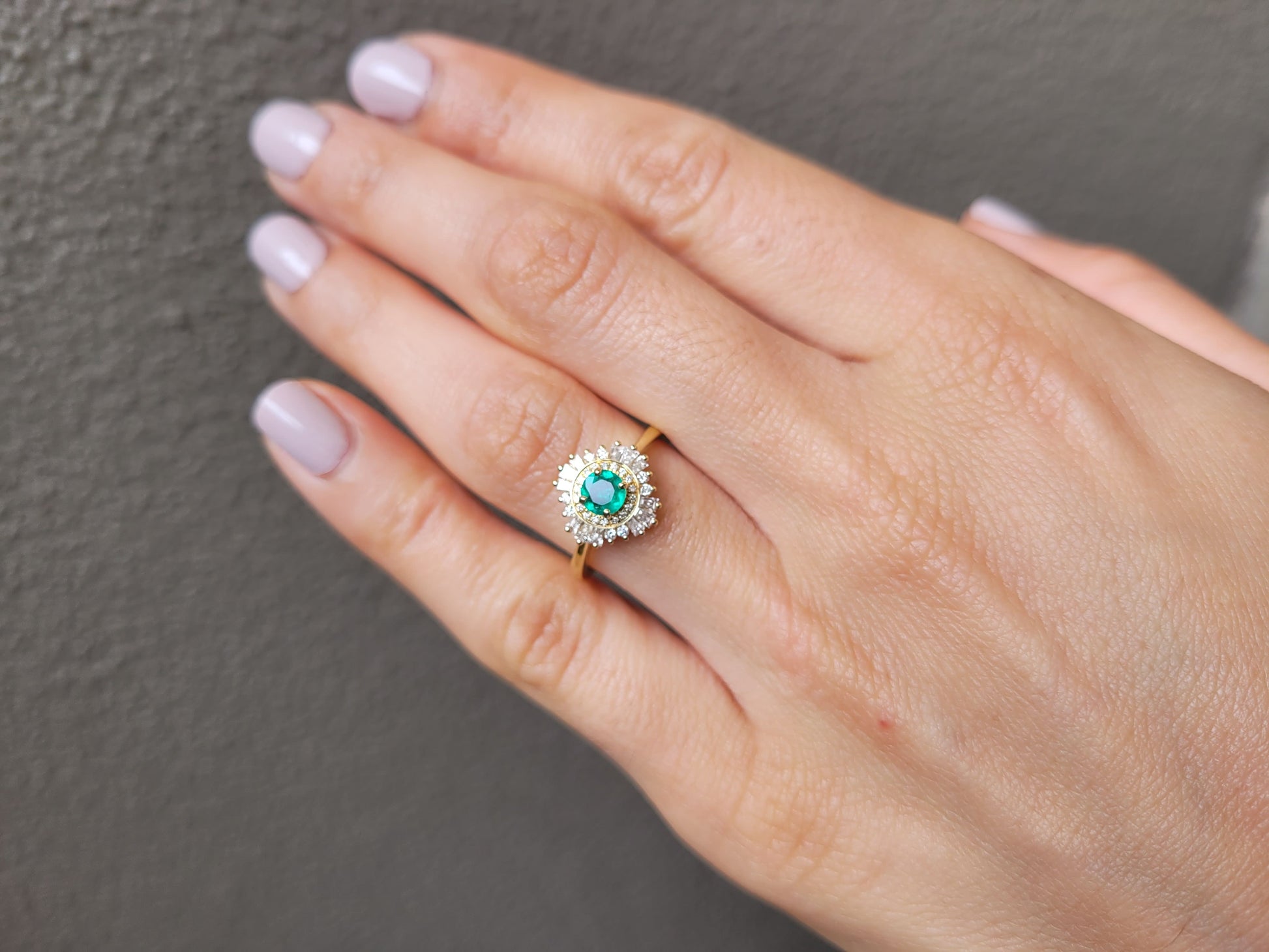 photo on hand of emerald Art Deco ring with diamond halo in light gray background