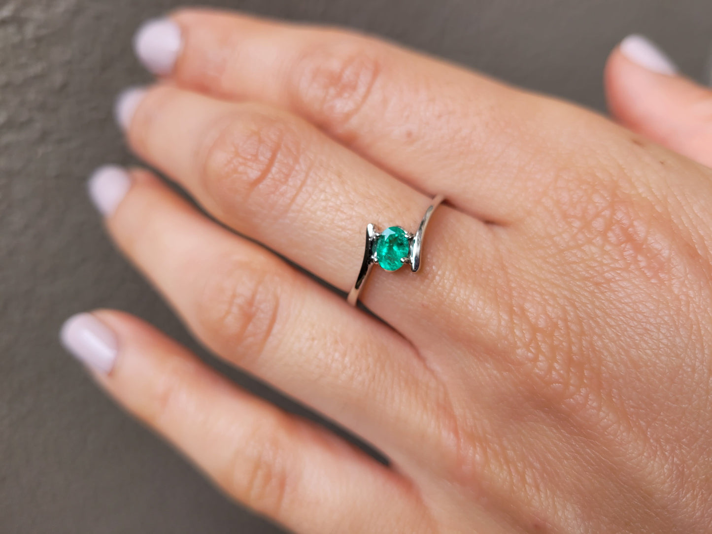 photo on hand of white gold ring with natural Colombian emerald in light gray background