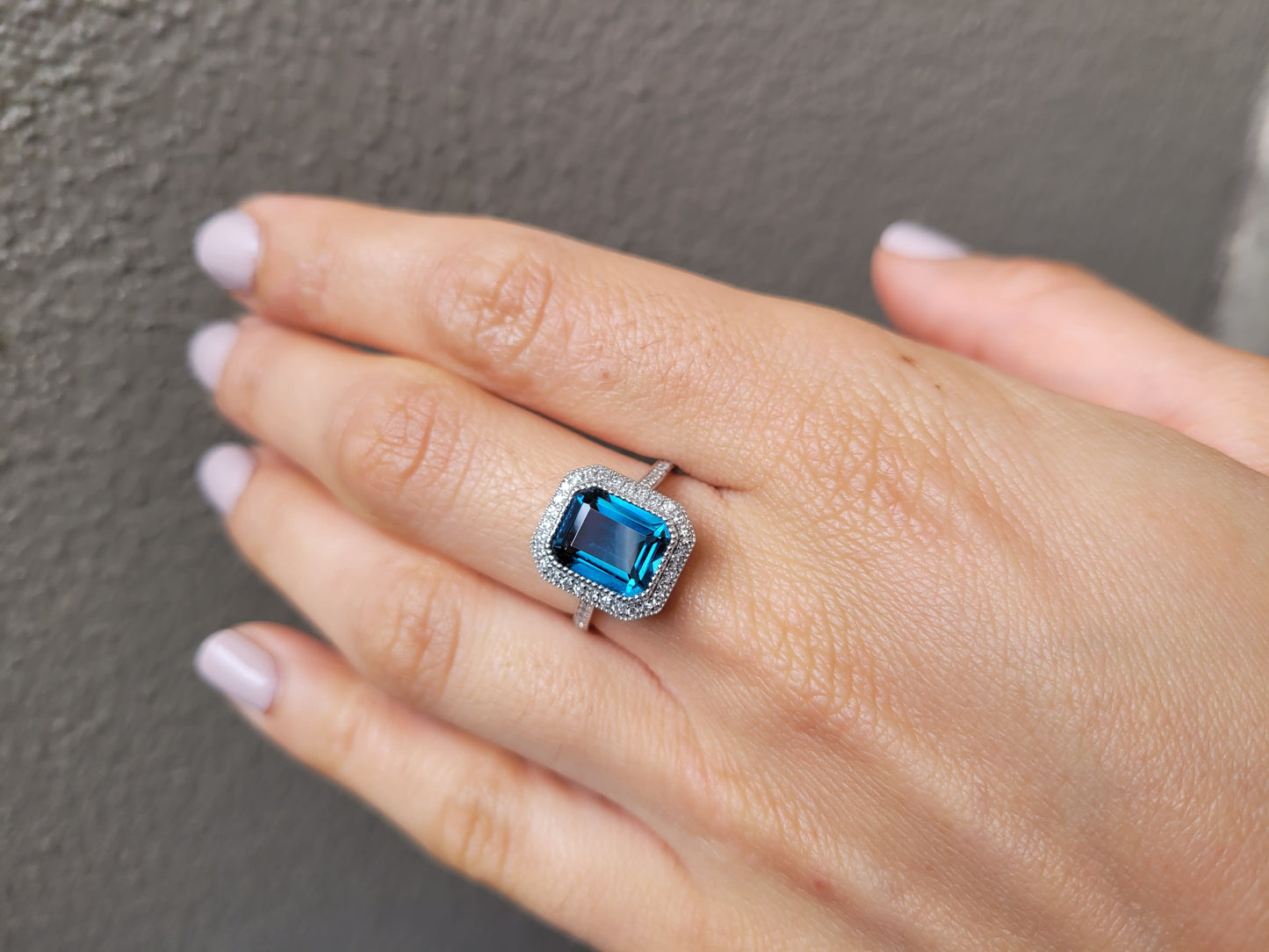 photo on white gold ring with London blue topaz and diamond halo in gray background