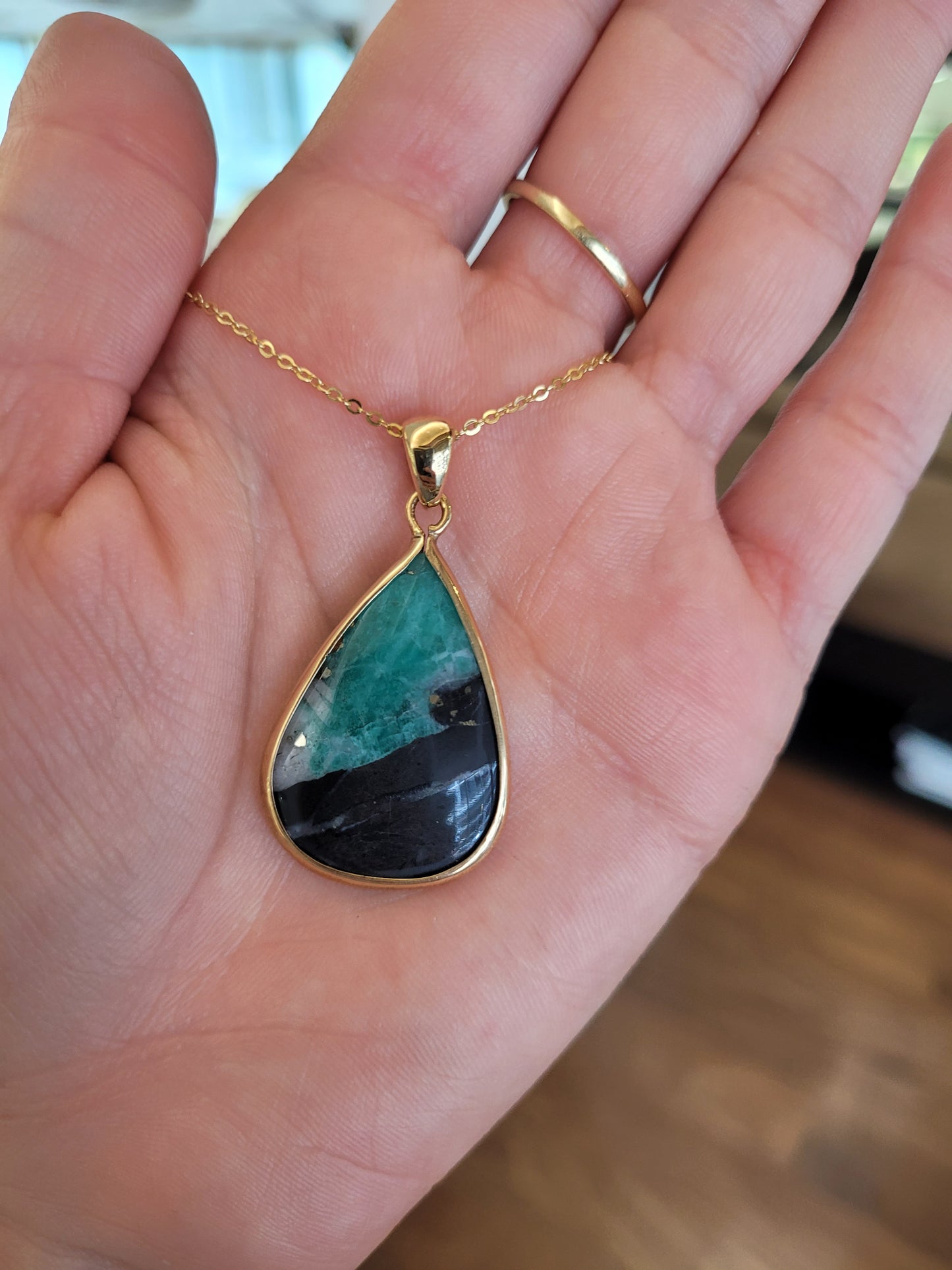 view on hand of emerald in matrix gold pendant on light gray background