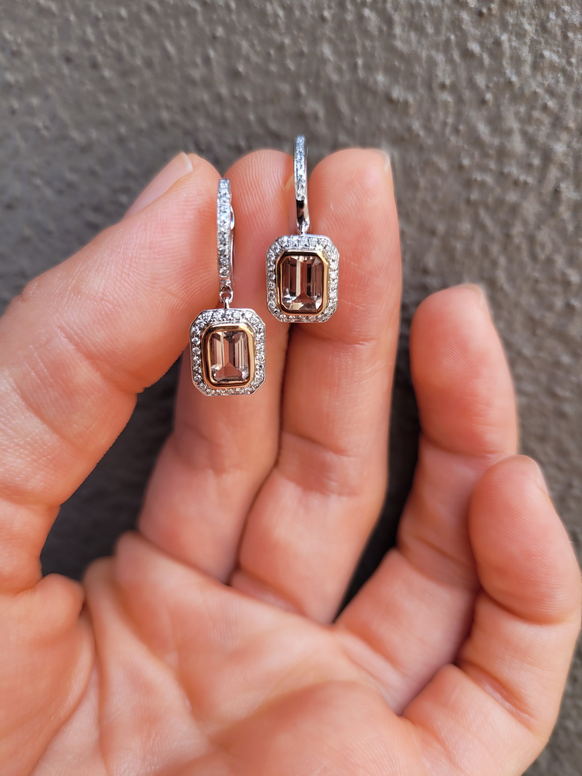 photo on hand of morganite and diamonds gold earrings in light gray background