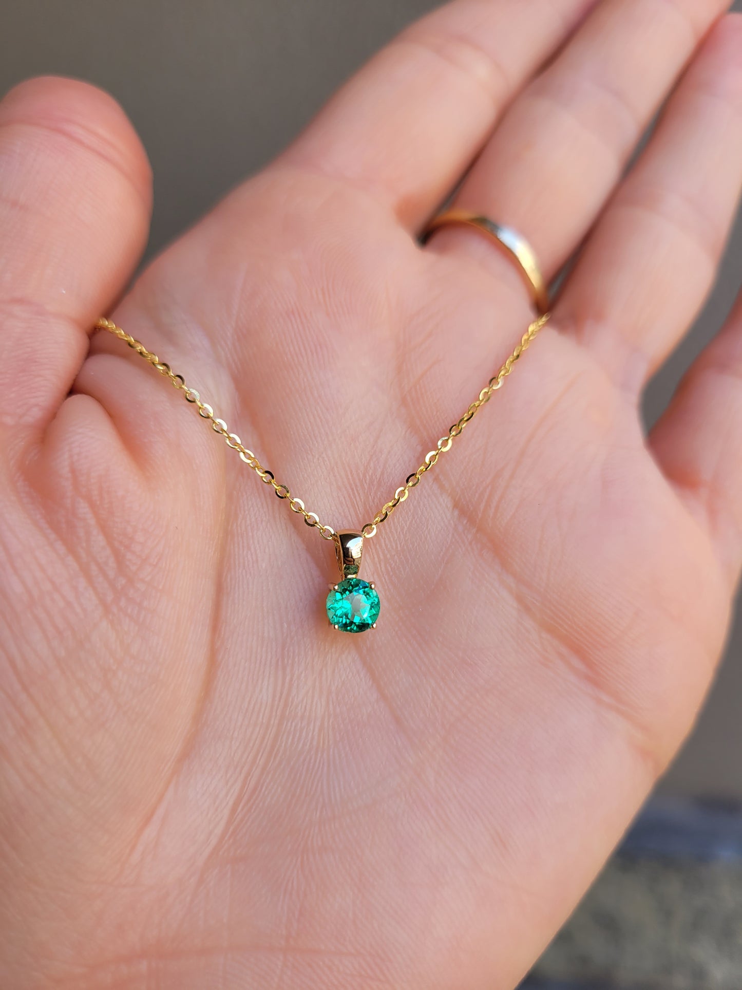 photo on hand of Colombian emerald gold pendant in gray background