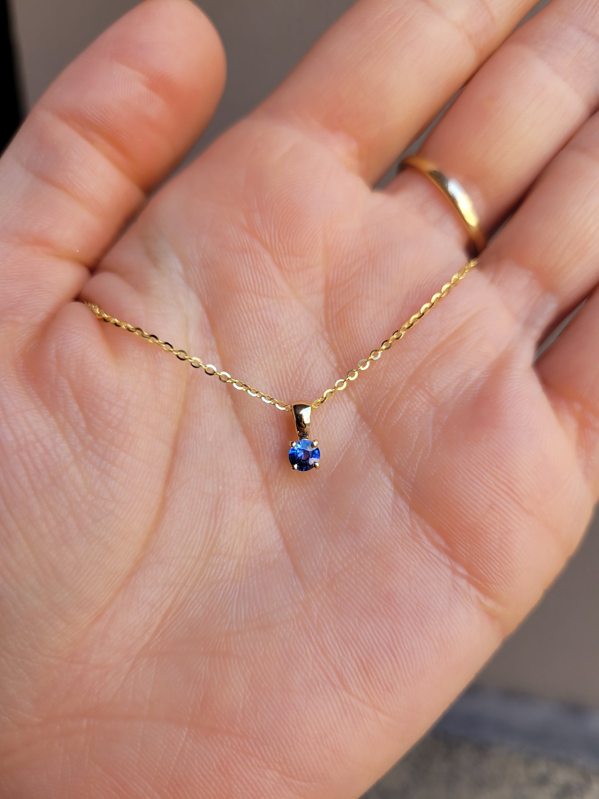 photo of yellow gold royal blue sapphire pendant in gray background against skin