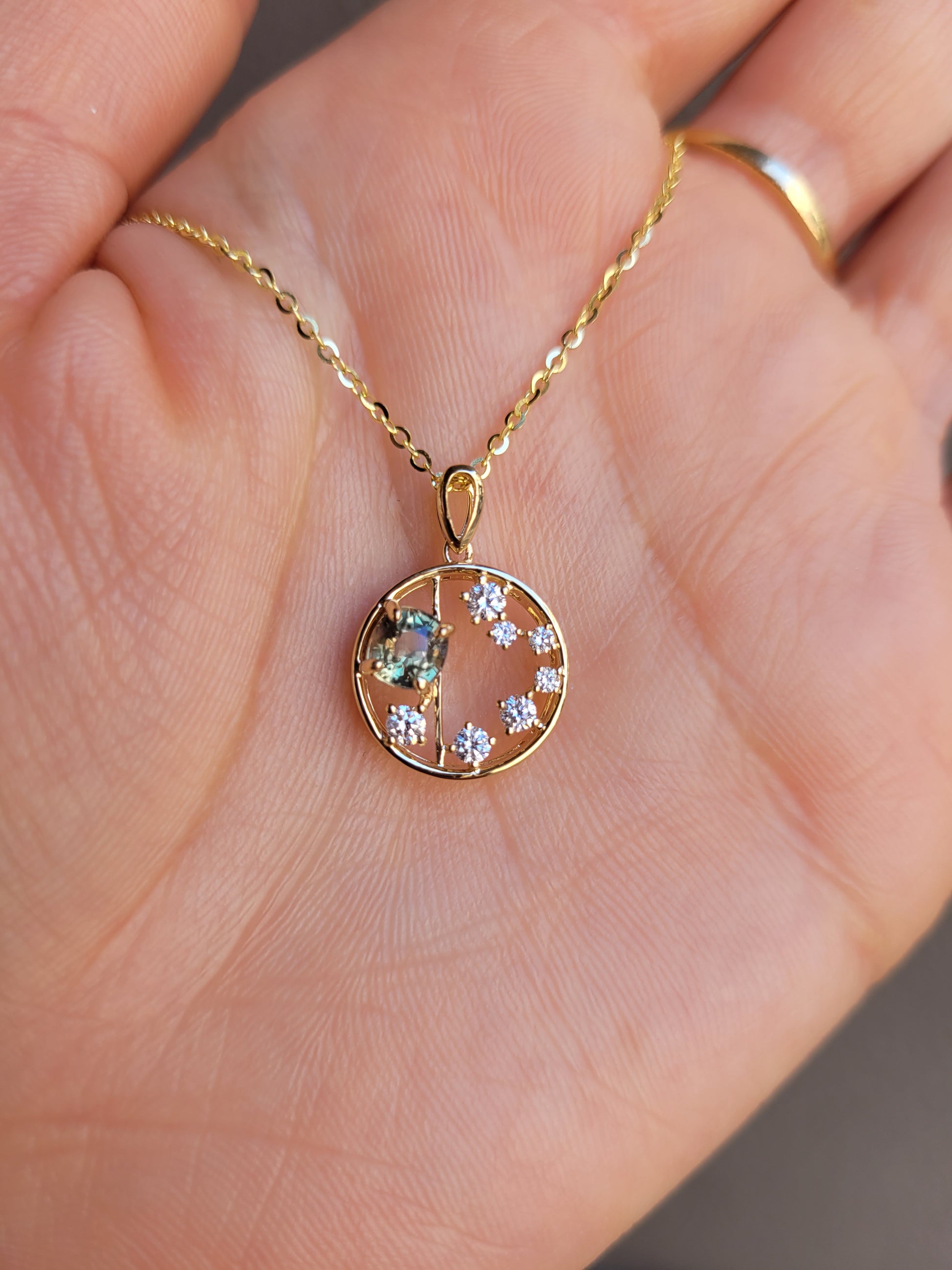photo on hand of circle gold pendant with alexandrite gemstone and small diamonds on a gray background