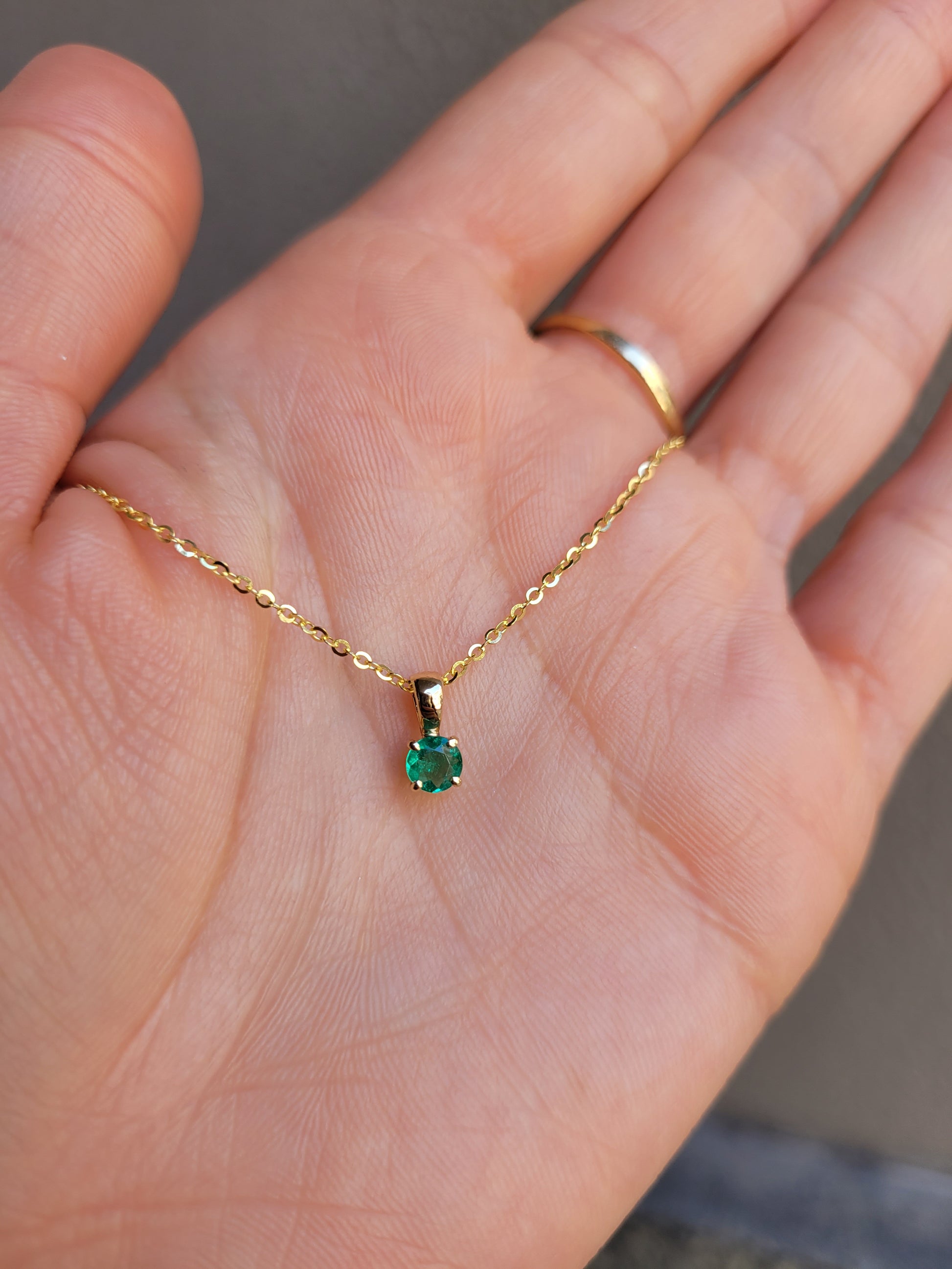 photo on hand of petite emerald pendant in gold in gray background 