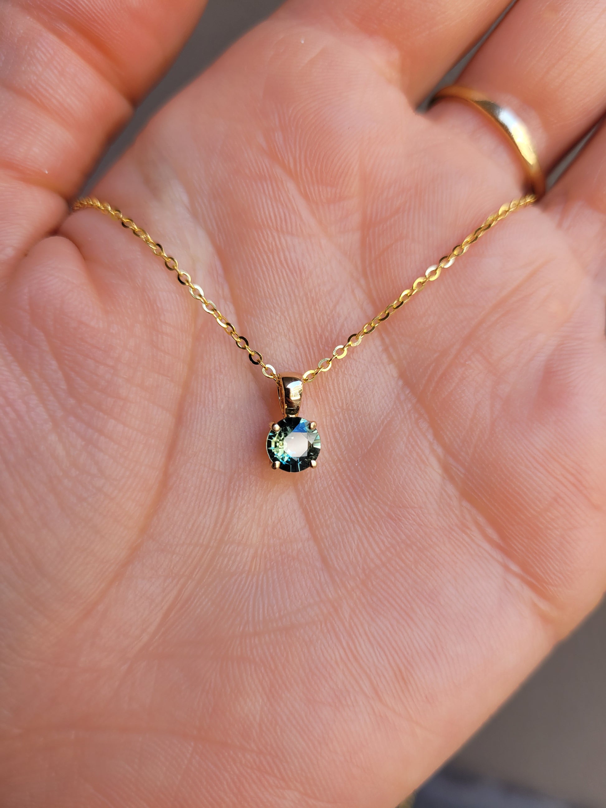 photo on hand of Australian teal sapphire pendant in 18K yellow gold