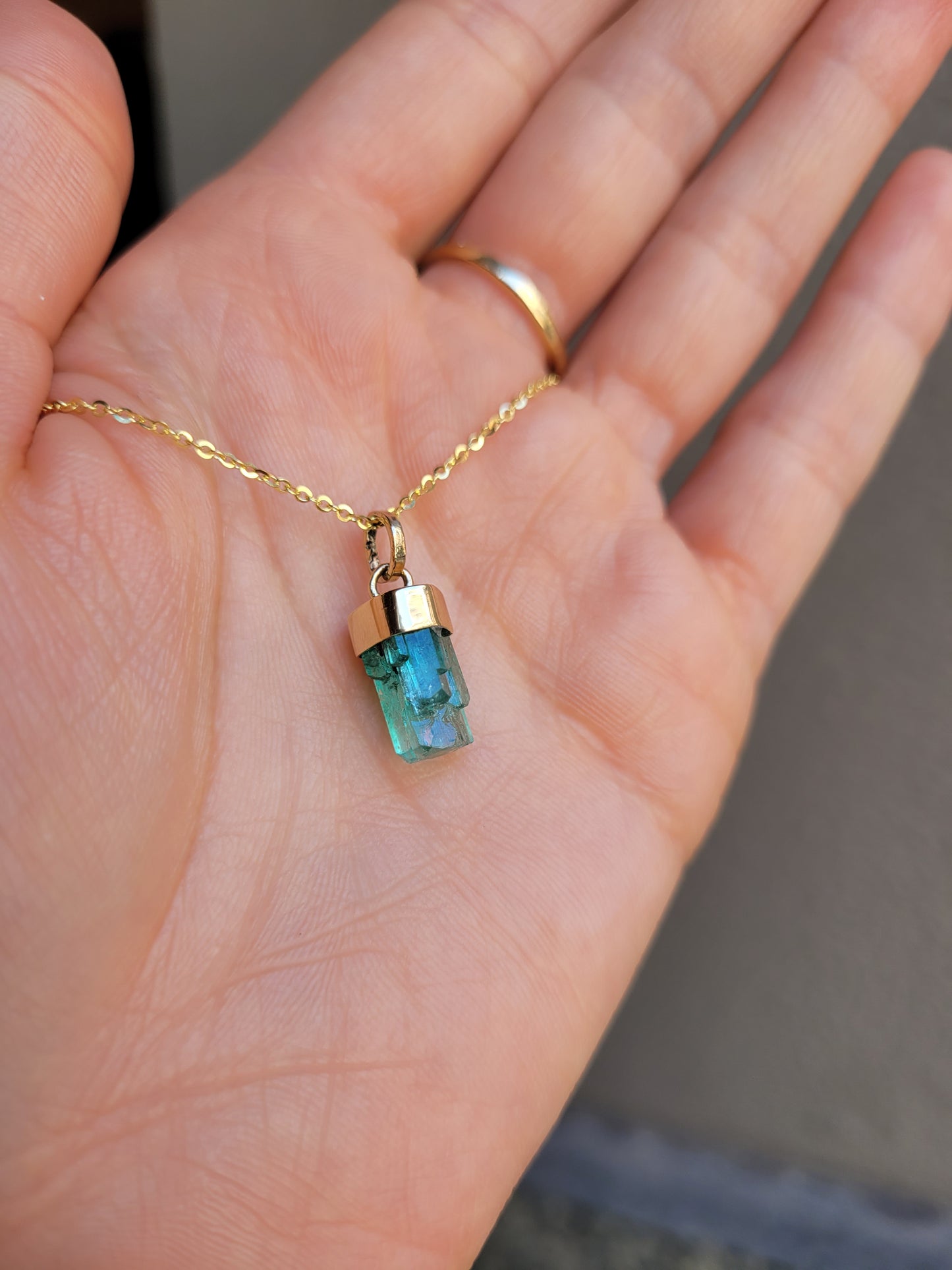 photo on hand of gold pendant with a rough emerald crystal on a light gray background