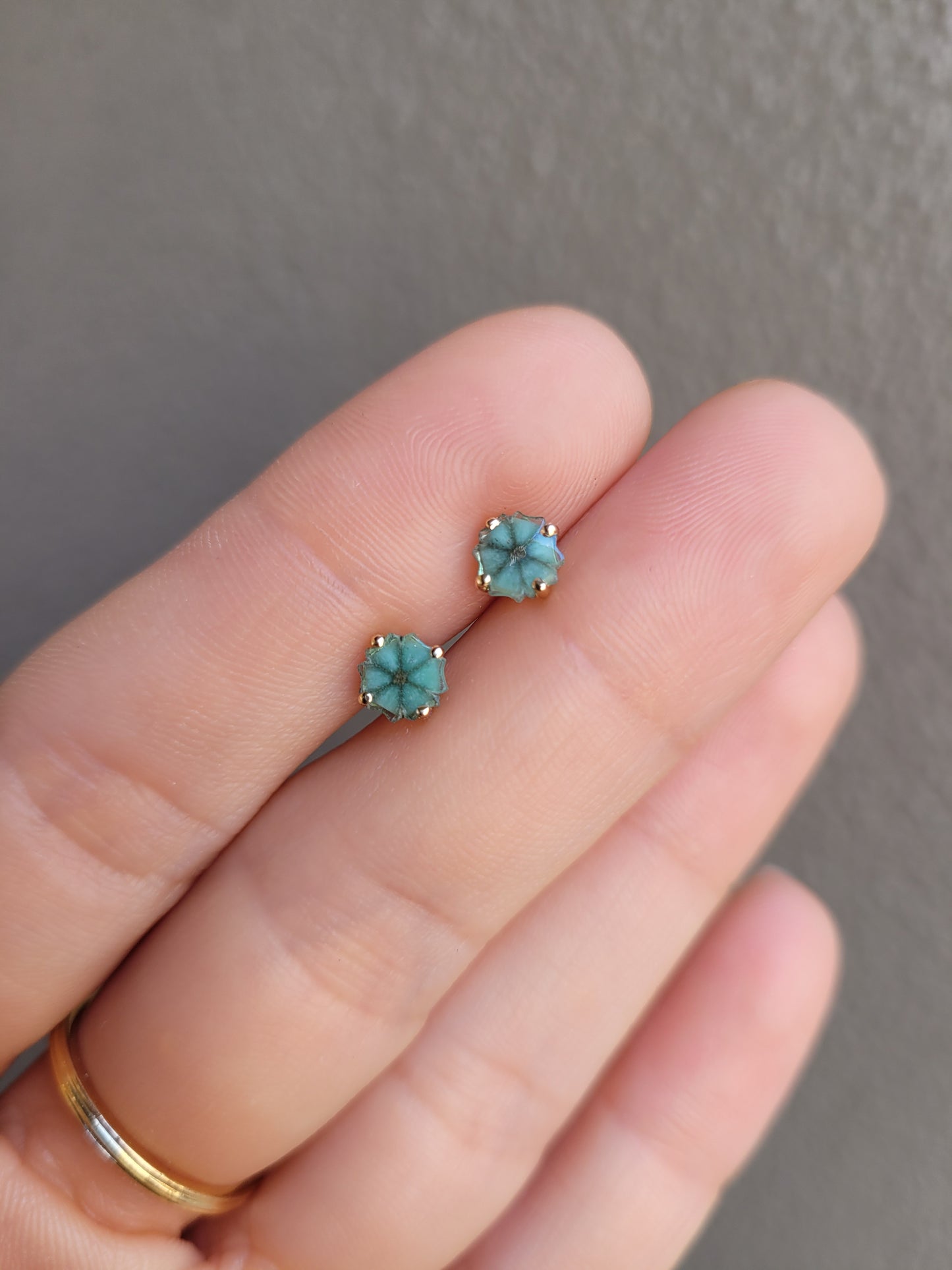 view on hand of pair of natural emerald stud earrings set in  18K yellow gold