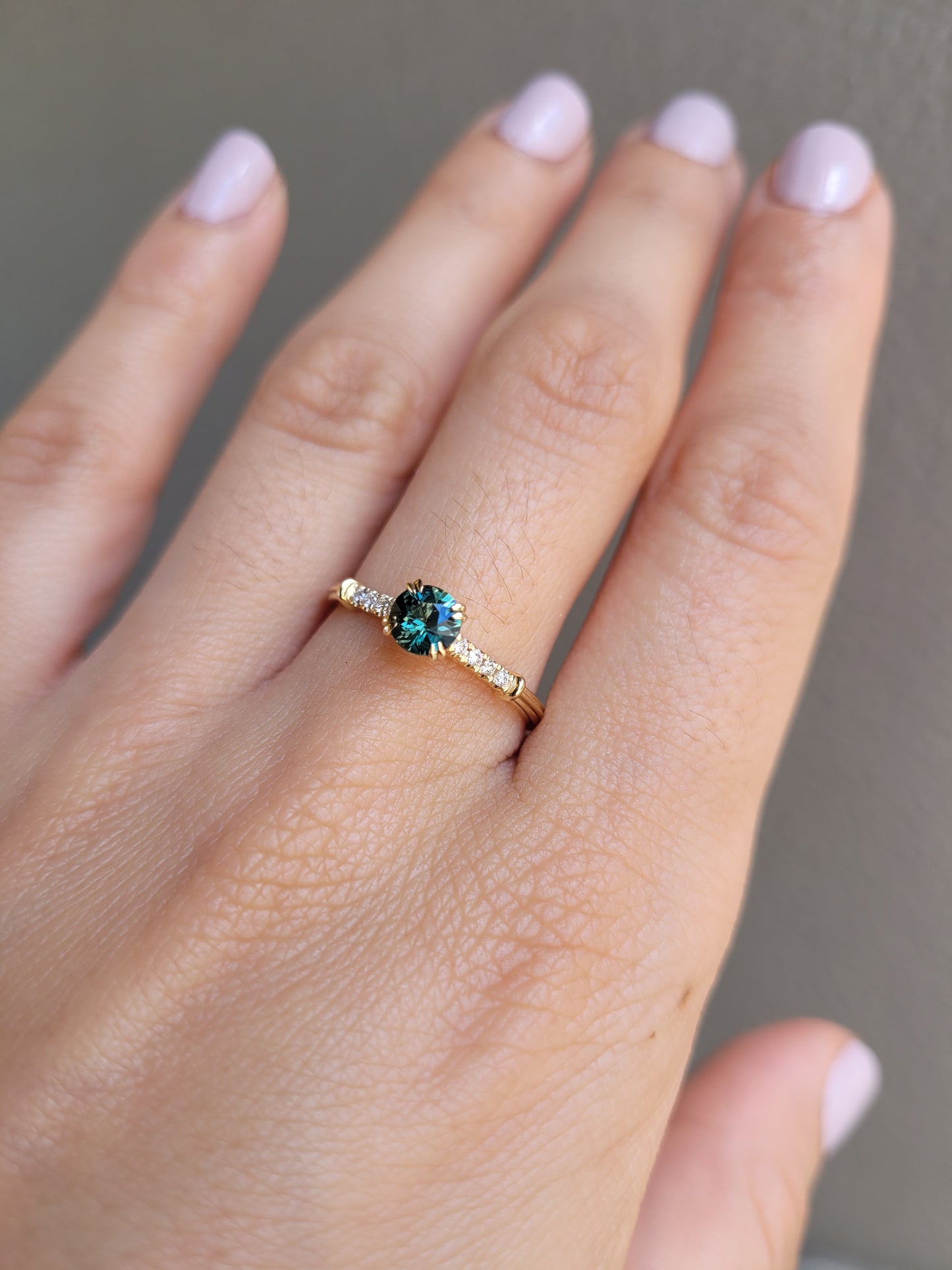 photo on hand of Round Australian Teal Sapphire Ring with Diamond Band in neutral background