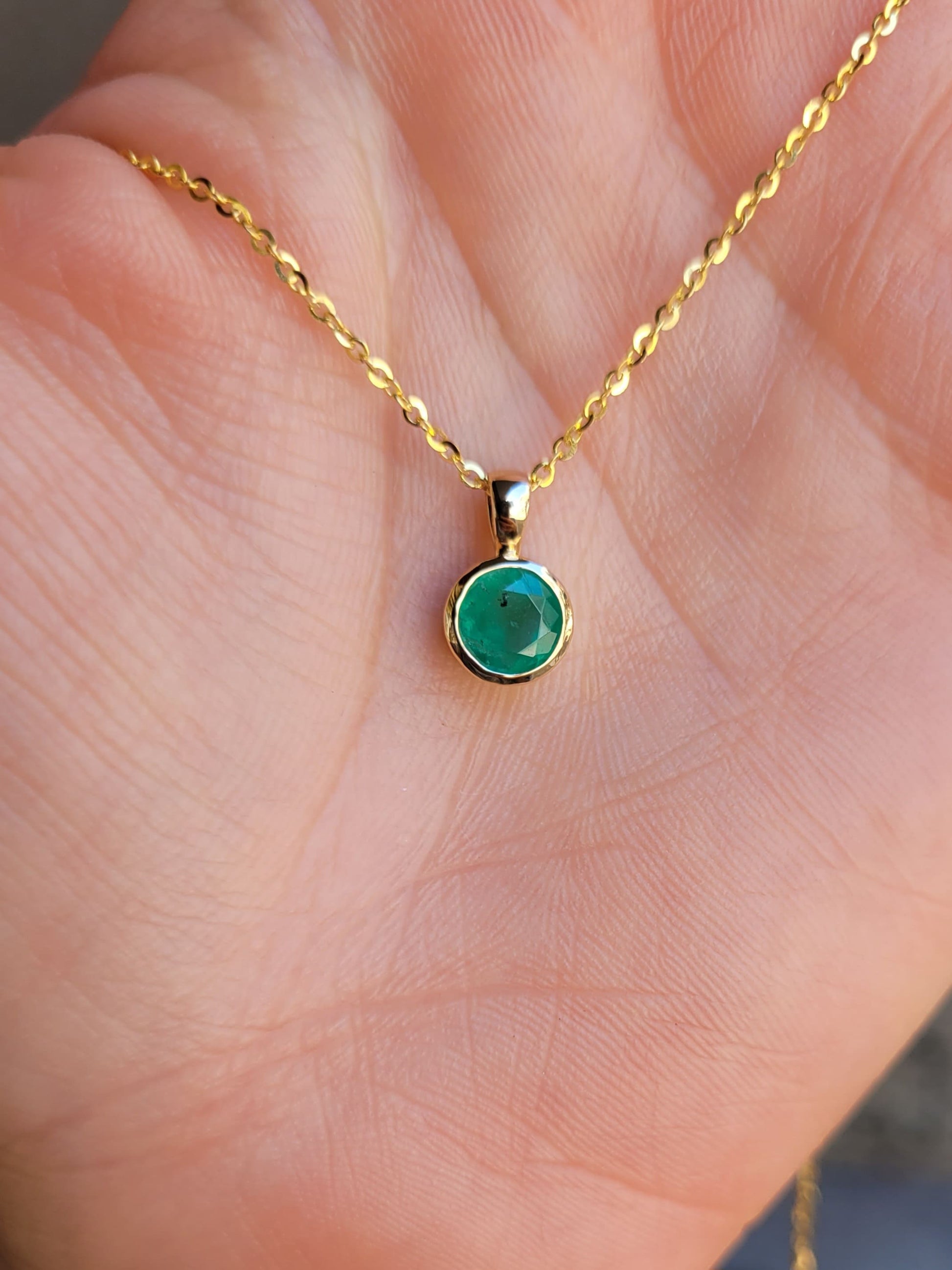 front view of Round Colombian Emerald Bezel Set Pendant in 18K Yellow Gold – 0.62ct held on hand
