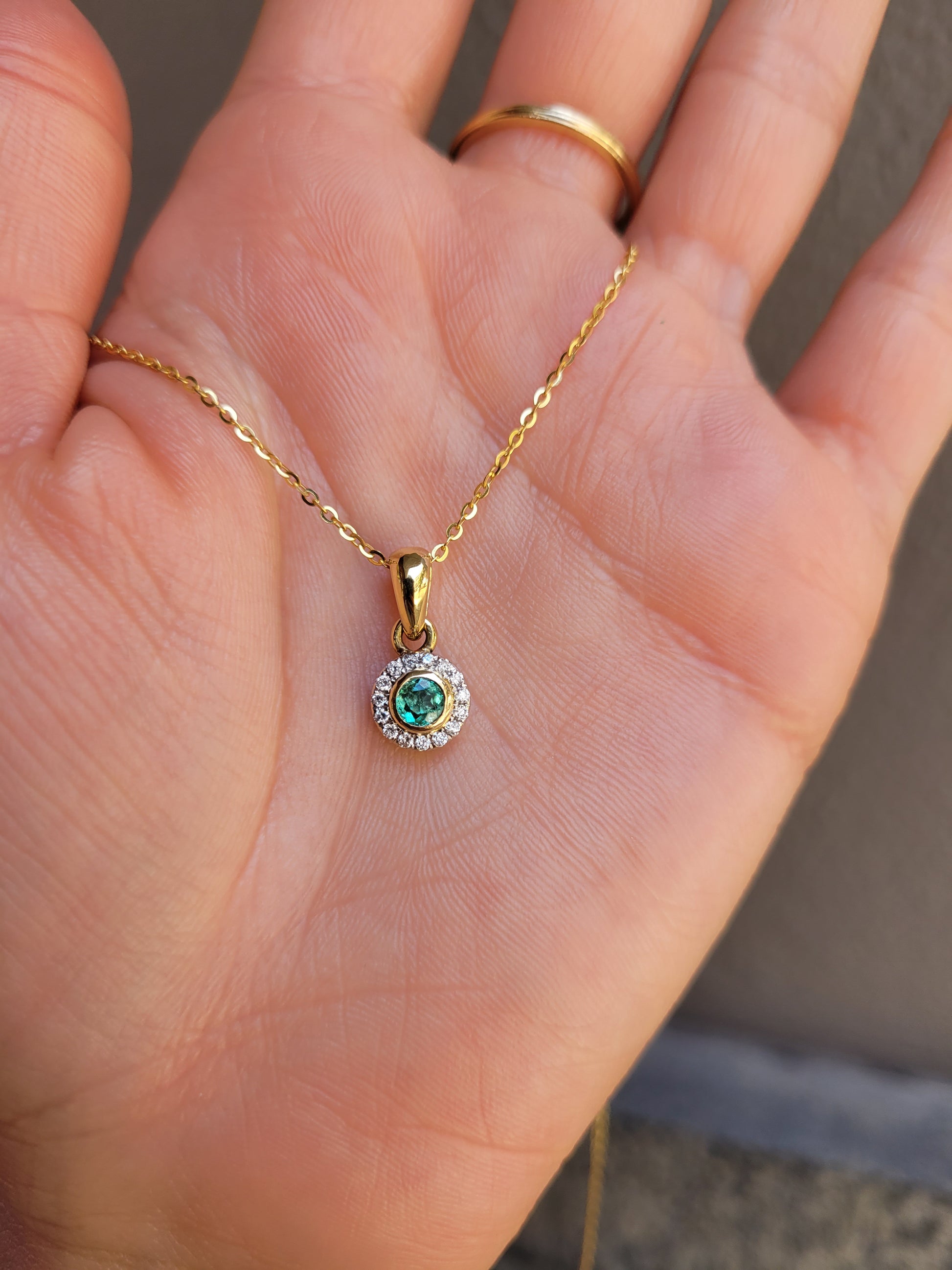 Natural Colombian Emerald and Diamond Halo pendant on a hand