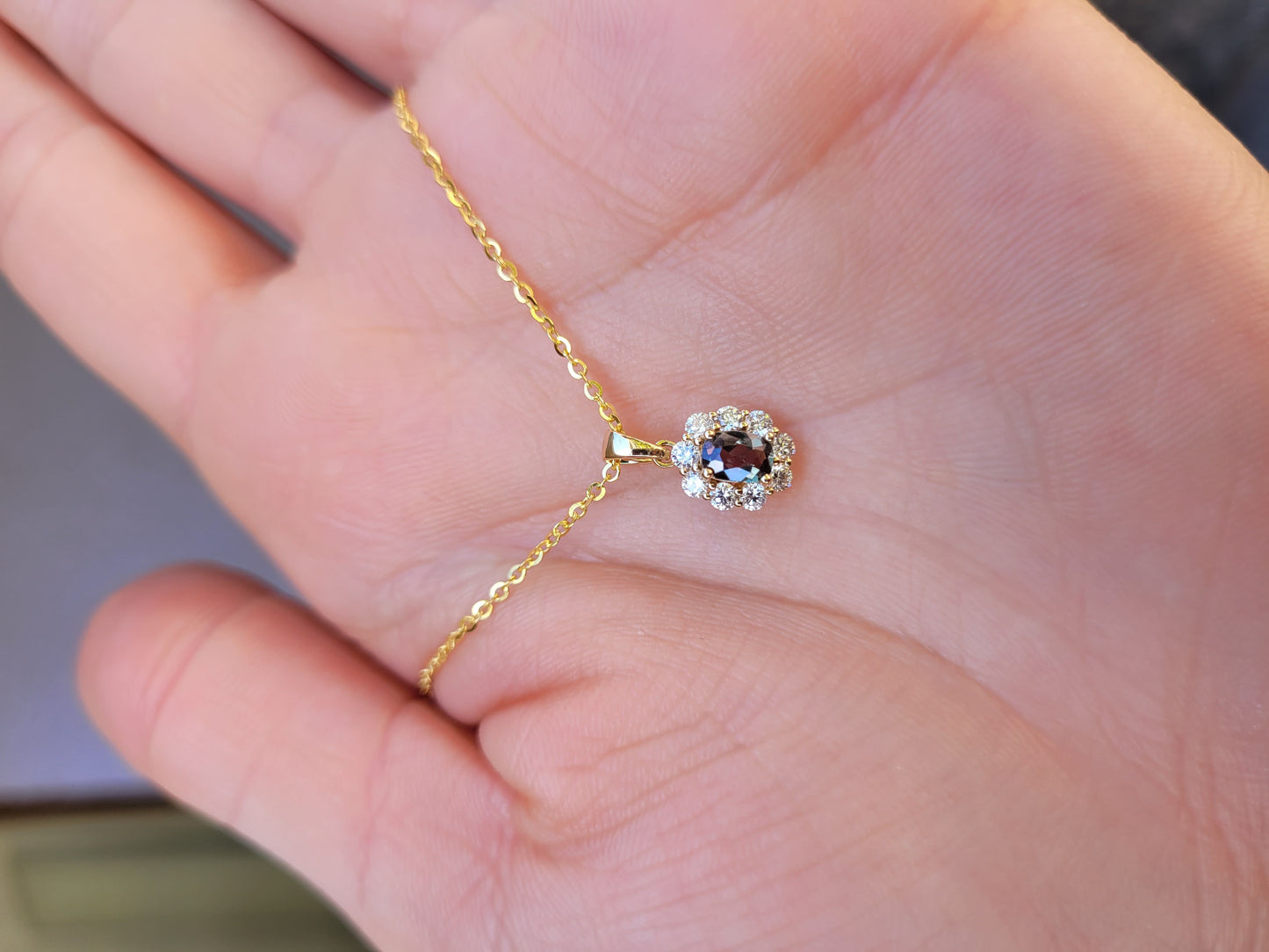 front view of Natural Alexandrite Halo Pendant 0.34ct Oval Cut in 18K Yellow Gold in neutral background held in a hand