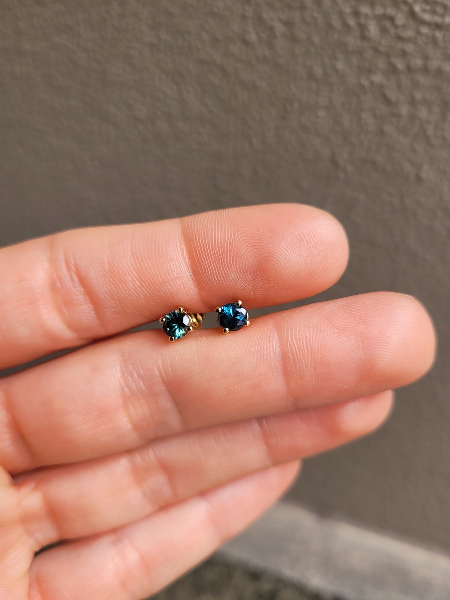 photo of hand holding a pair of round natural Australian teal sapphire studs in neutral background