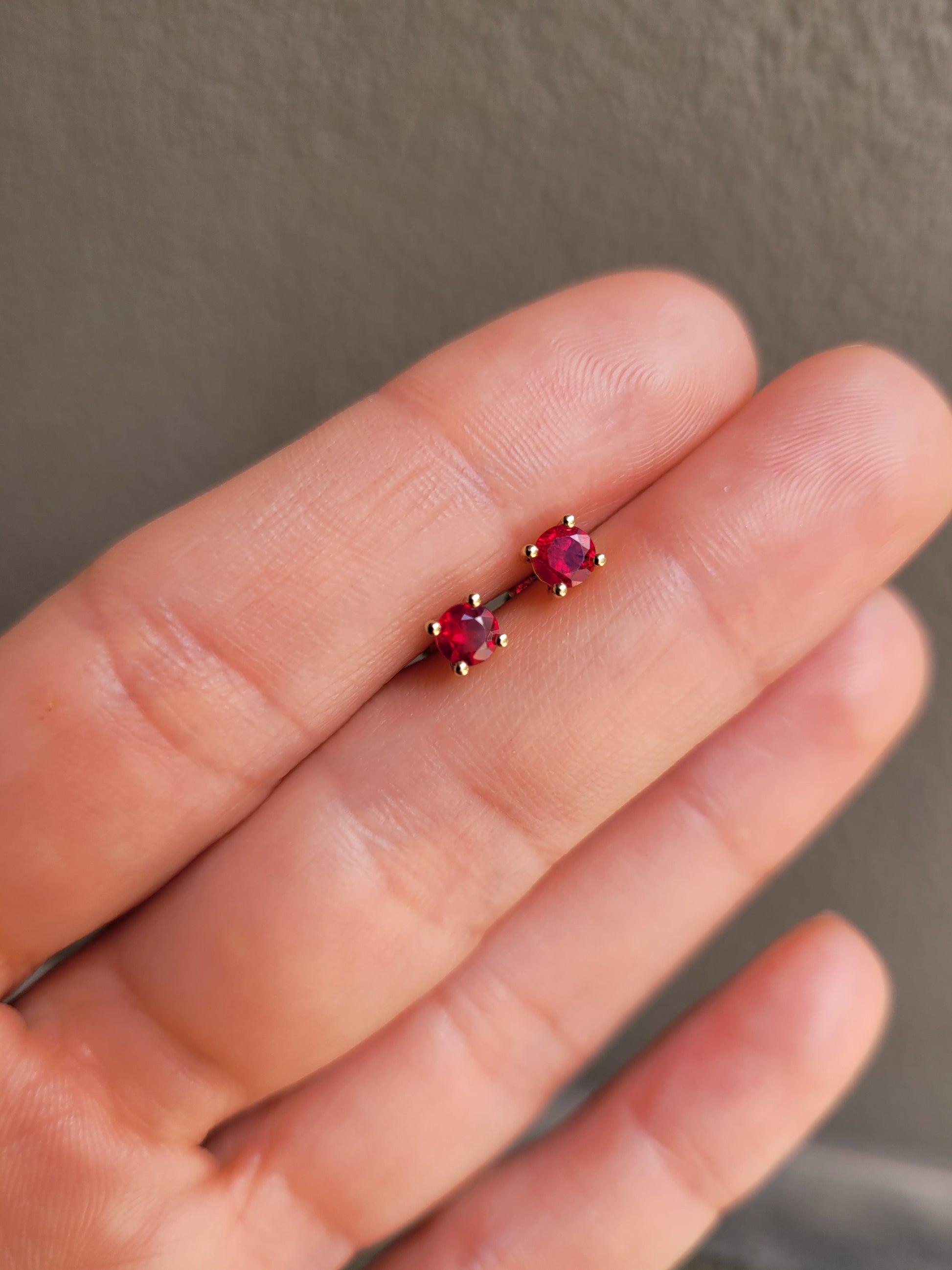 video of Natural Ruby Stud Earrings in 18K Yellow Gold held between fingers in neutral background