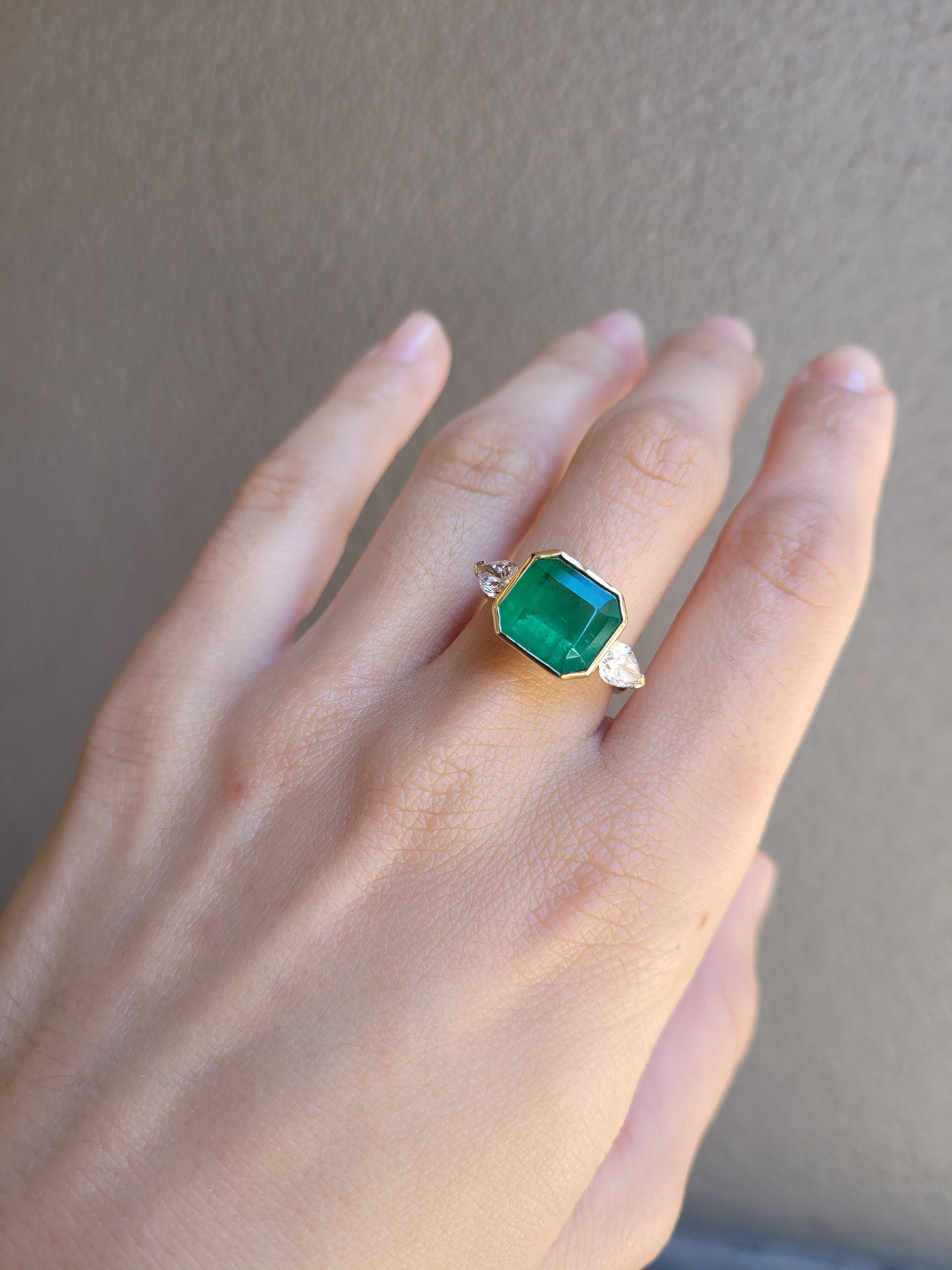 Hand wearing a Colombian Emerald and Diamond Ring in 18K Yellow Gold – East West Emerald Cut in neutral background 