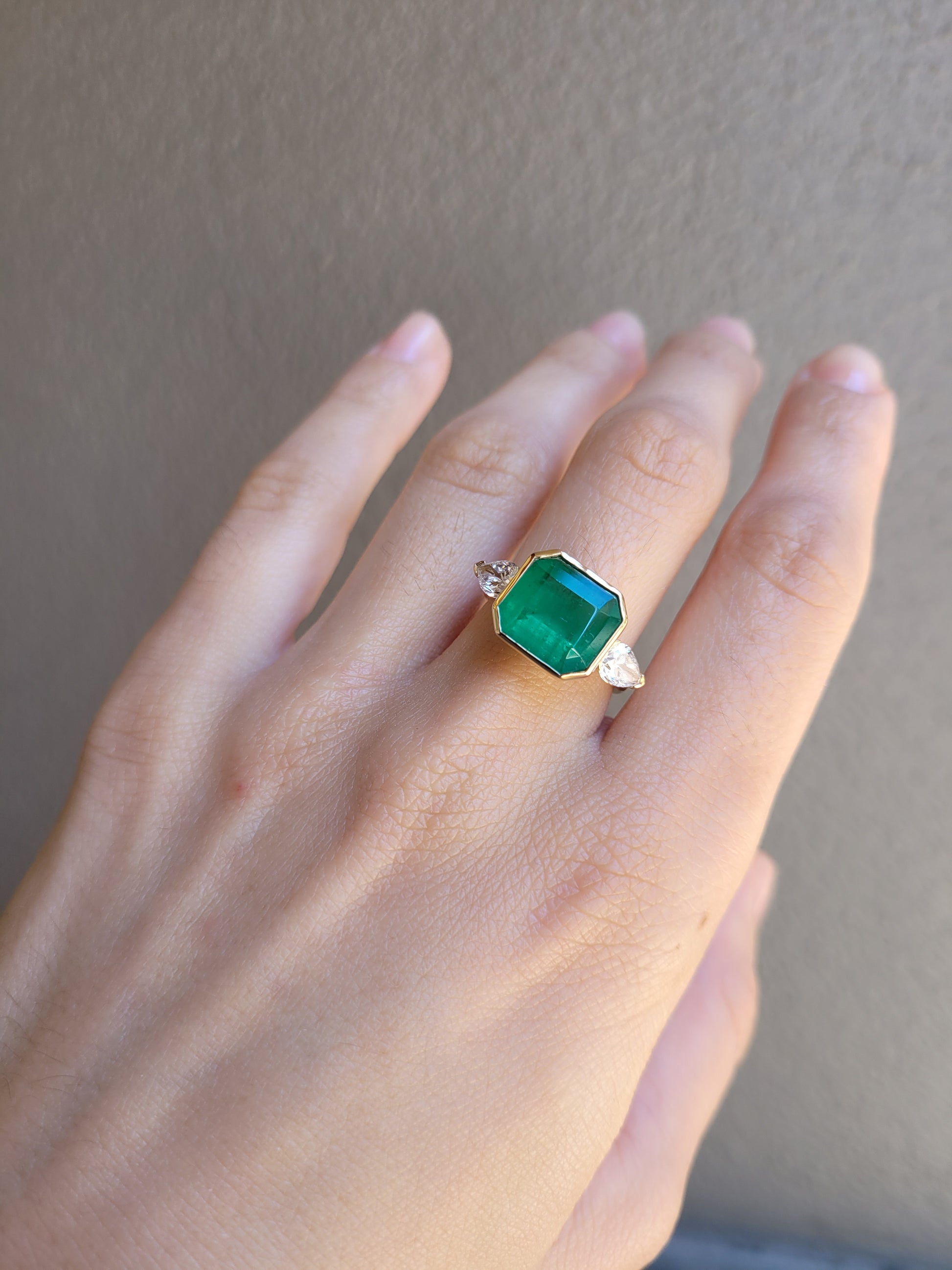 Hand wearing a Colombian Emerald and Diamond Ring in 18K Yellow Gold – East West Emerald Cut in neutral background 