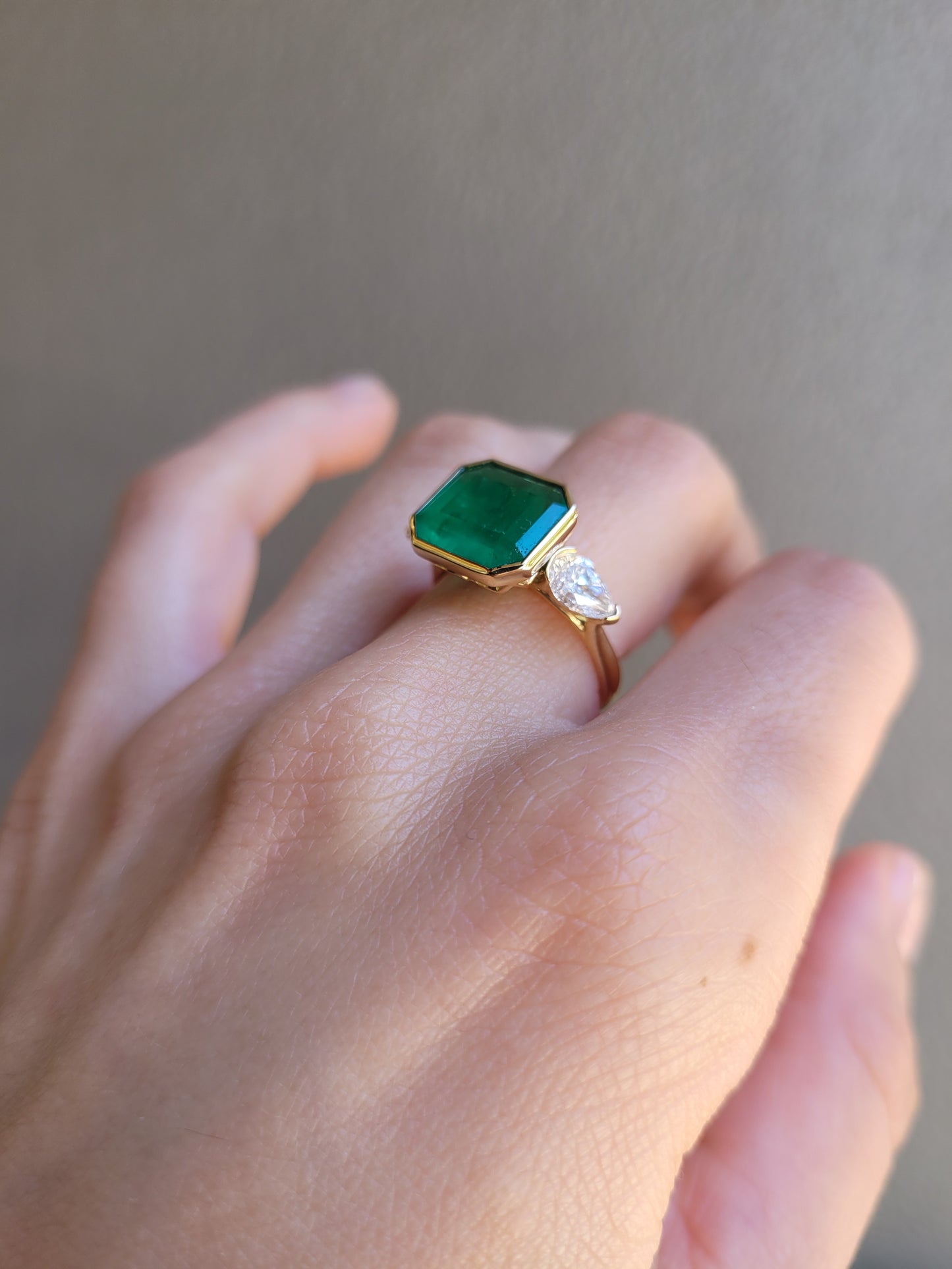side profile of a hand wearing a Colombian Emerald and Diamond Ring in 18K Yellow Gold – East West Emerald Cut in neutral background 