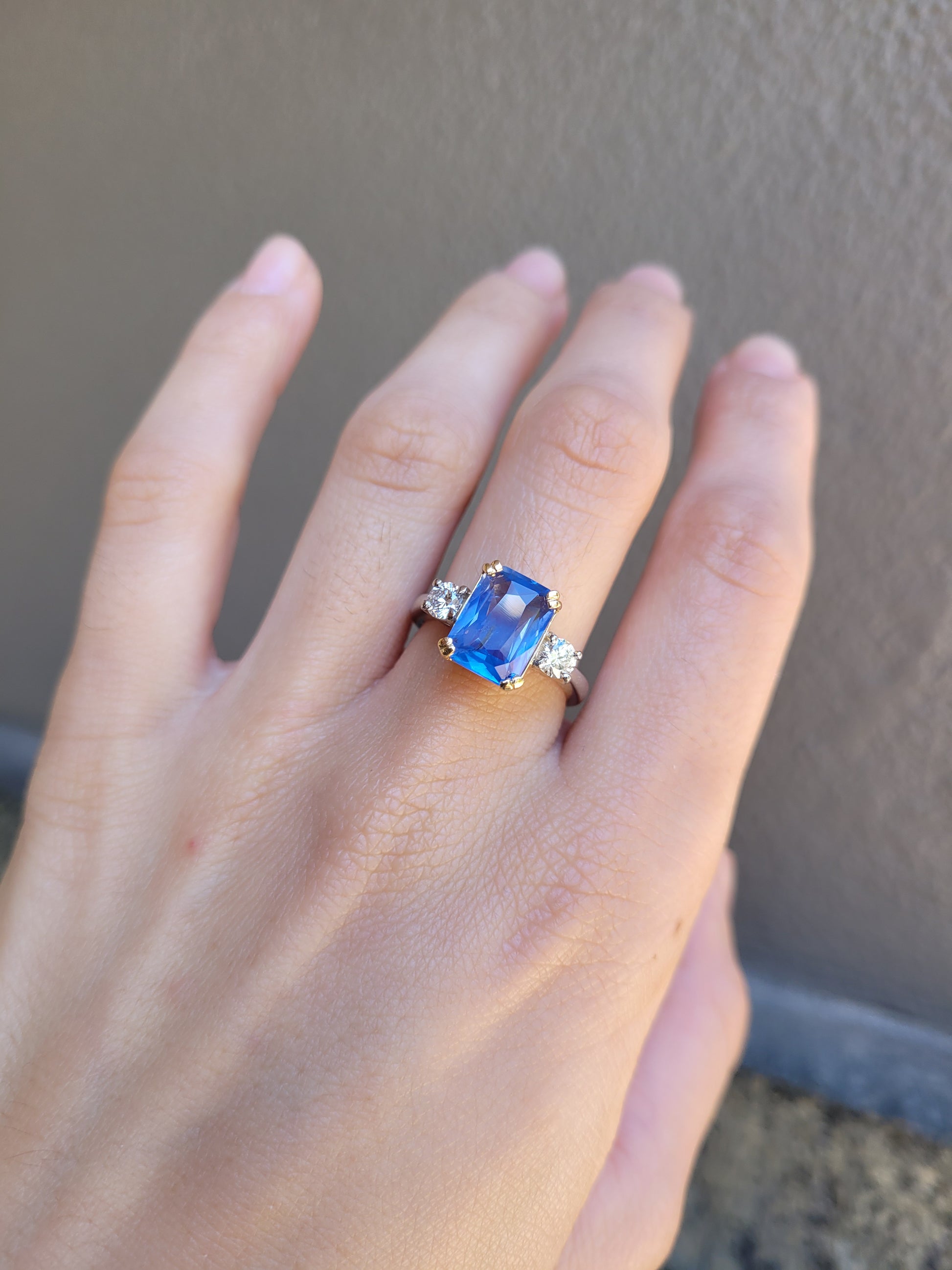 Hand wearing a ring with a 4.6ct blue sapphire on a neutral background