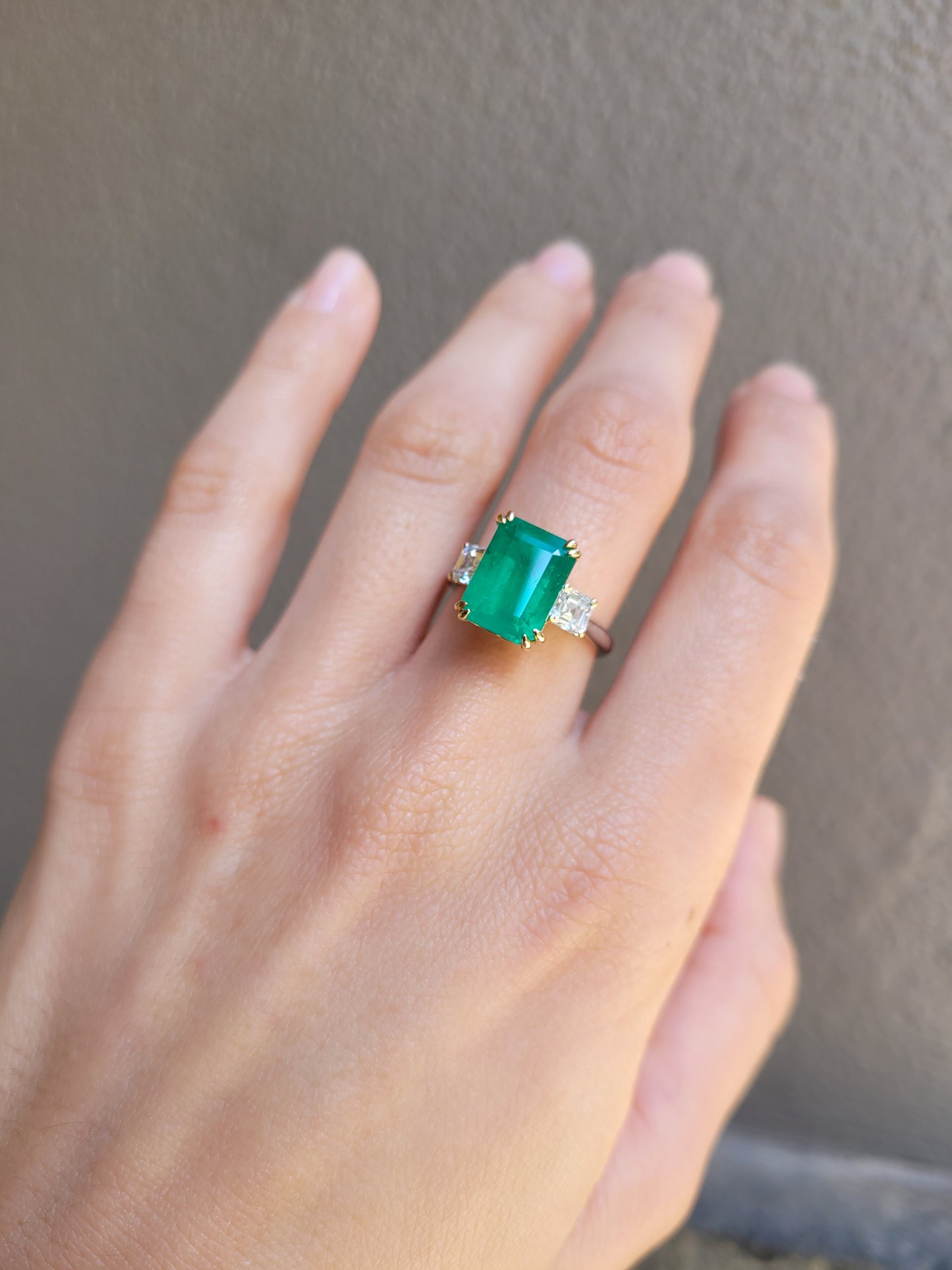 Hand wearing a Colombian Emerald and Diamond Ring in 18K Yellow Gold – East West Emerald Cut in neutral background