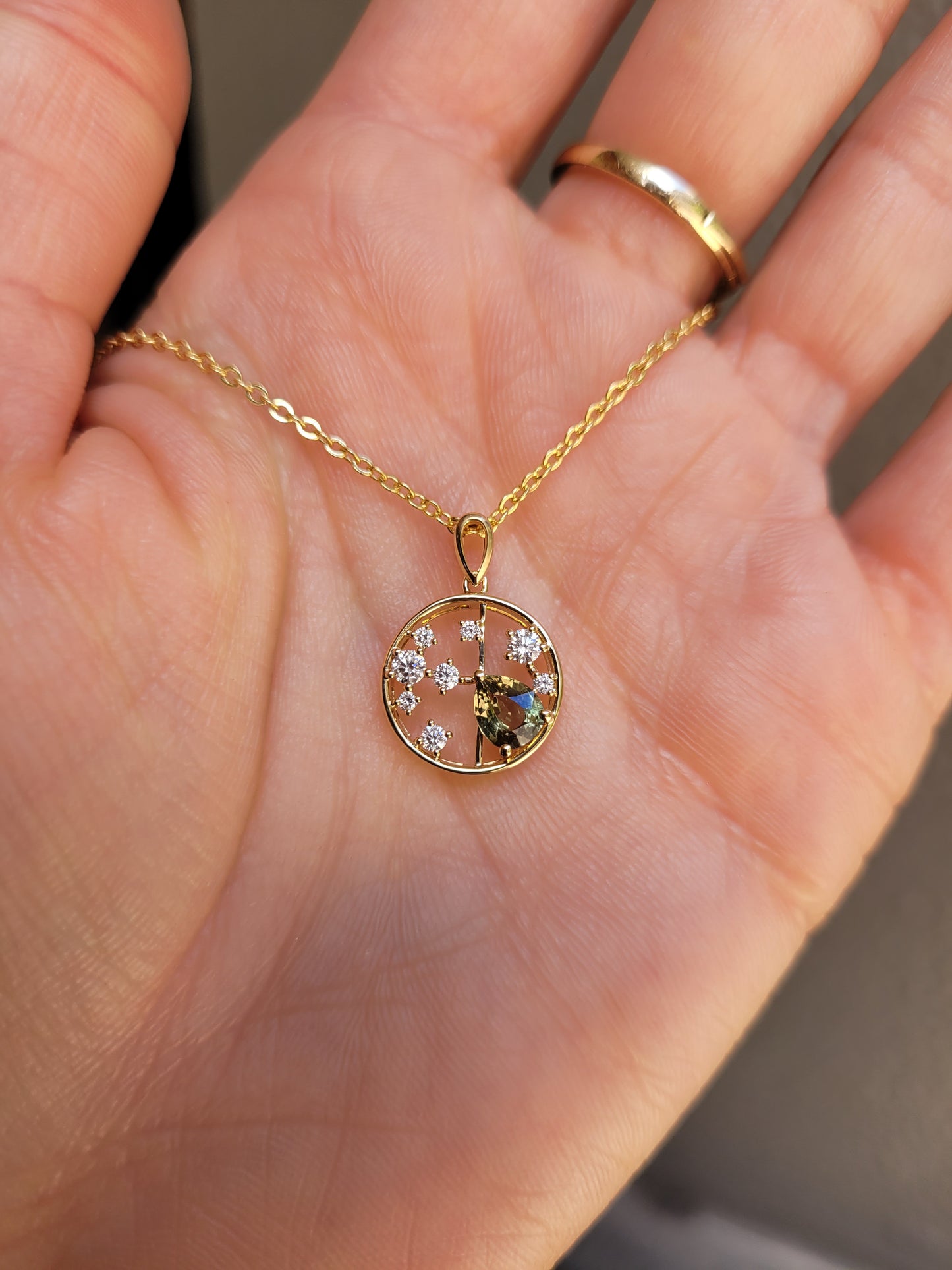 photo of hand holding a Natural Alexandrite and Diamond Pendant in 18K Yellow Gold – 0.63ct Pear Cut in neutral background