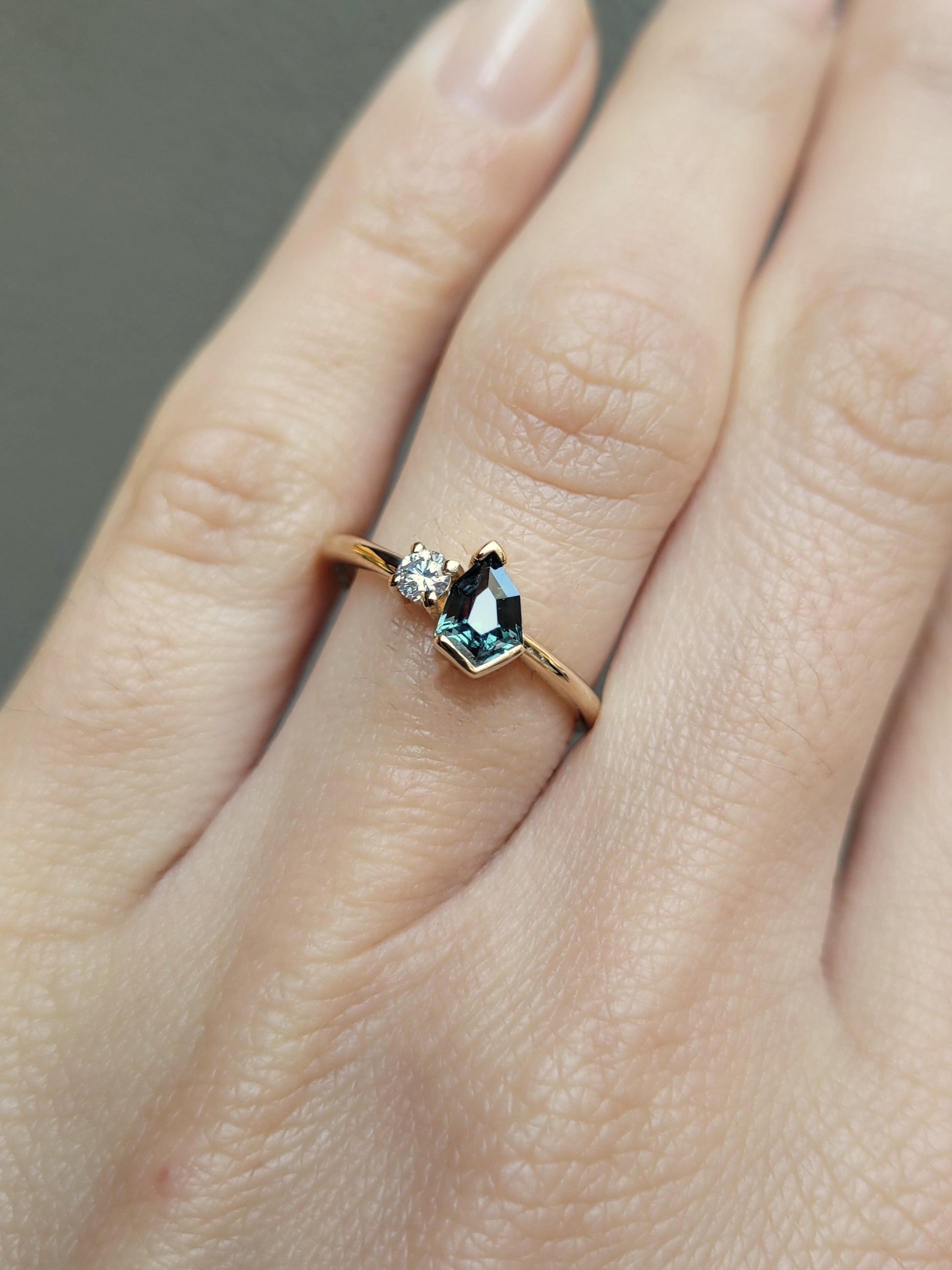 photo on hand of Teal Sapphire and Diamond Toi et Moi Ring in 18K Yellow Gold in neutral background 