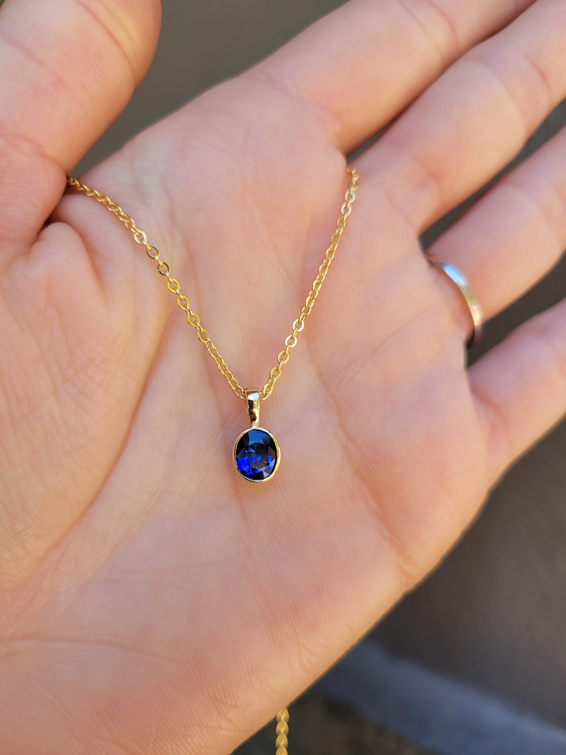 photo on hand of Royal Blue Sapphire Pendant in 18K Yellow Gold in neutral background