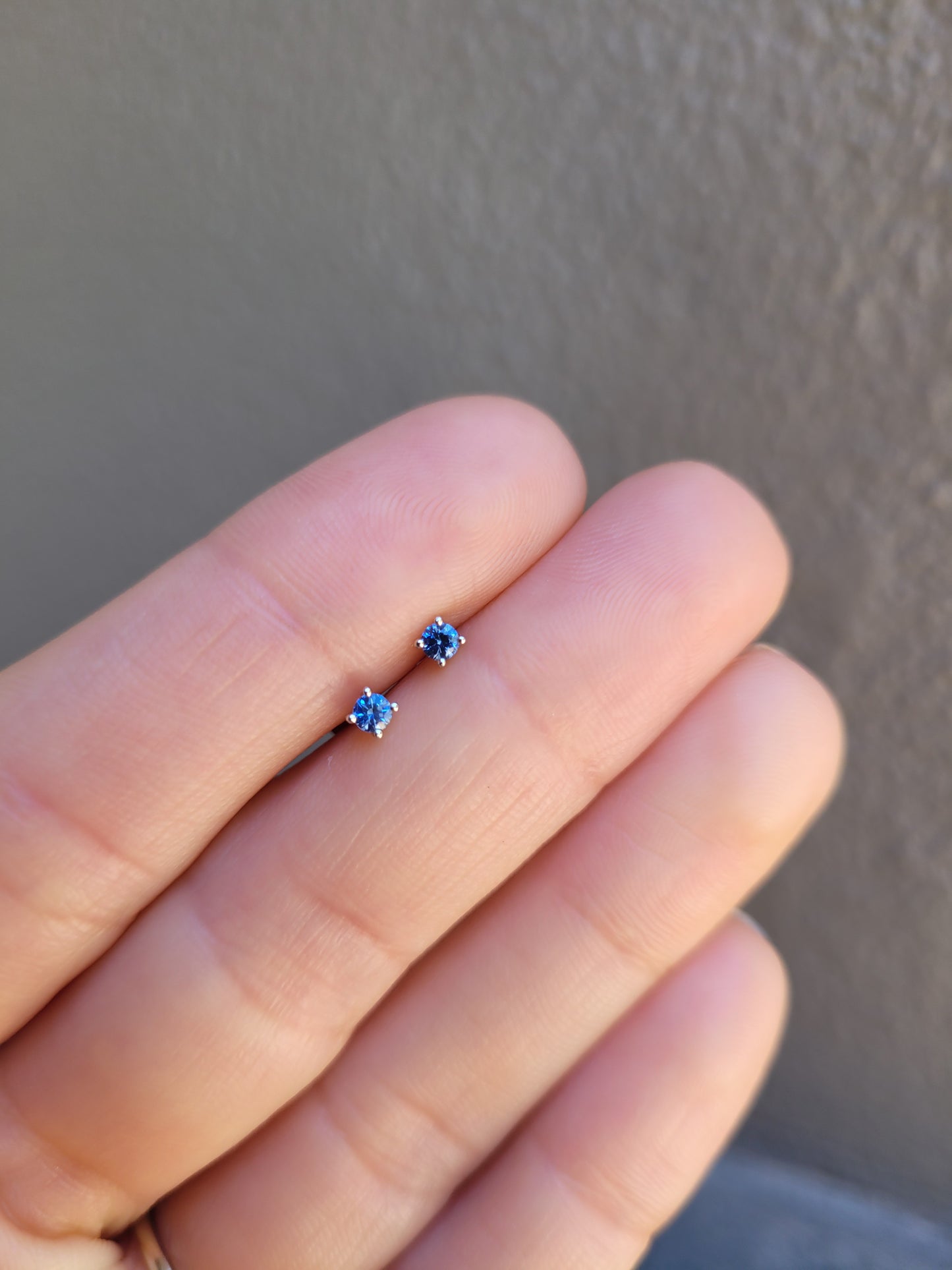 Small natural blue sapphire platinum earring held between fingers against a neutral background