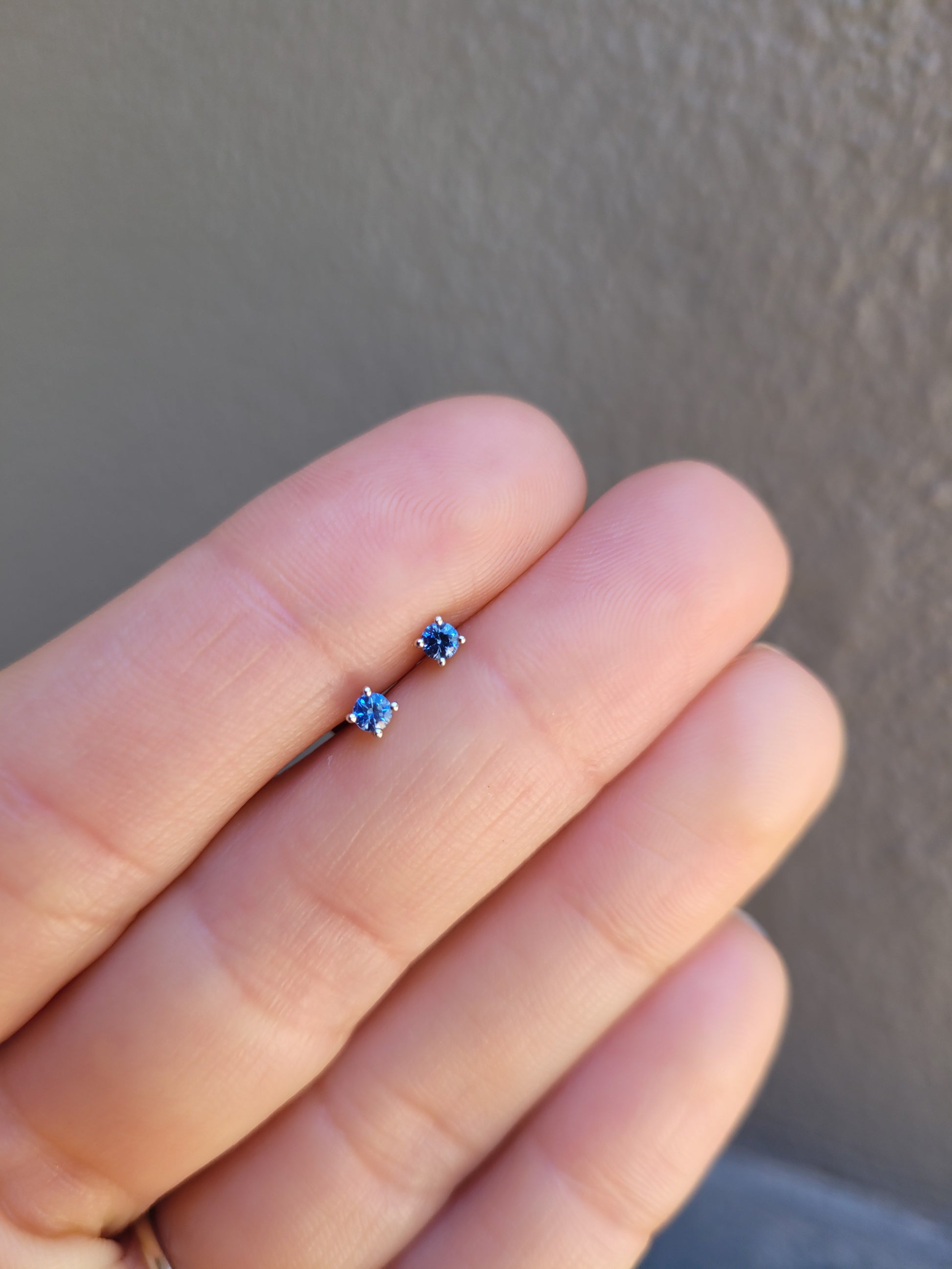 Small natural blue sapphire platinum earring held between fingers against a neutral background