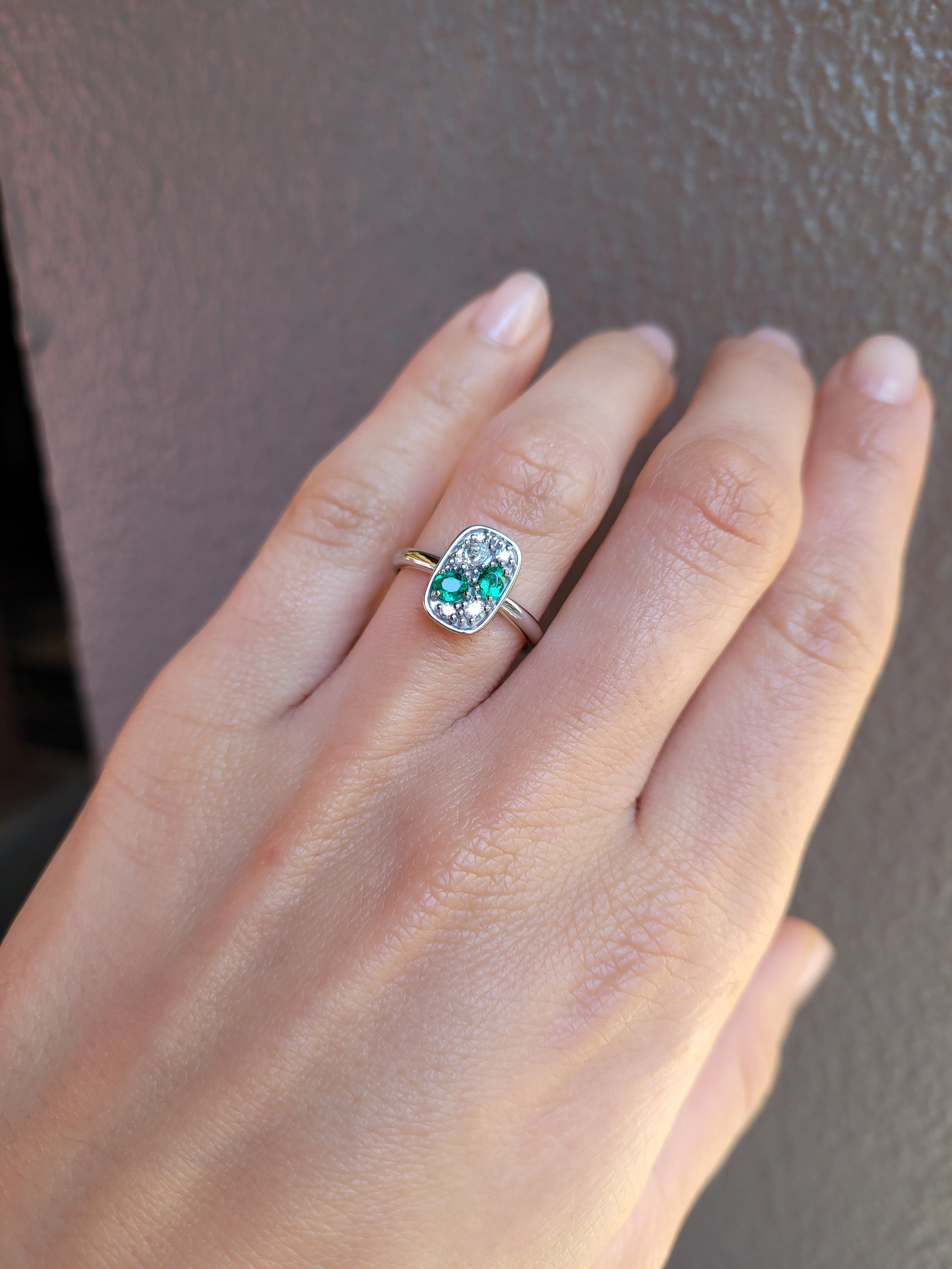 A close-up of a hand wearing a Natural Colombian Emerald & Diamond Composition Ring in Platinum in white background shown against a textured brown background.