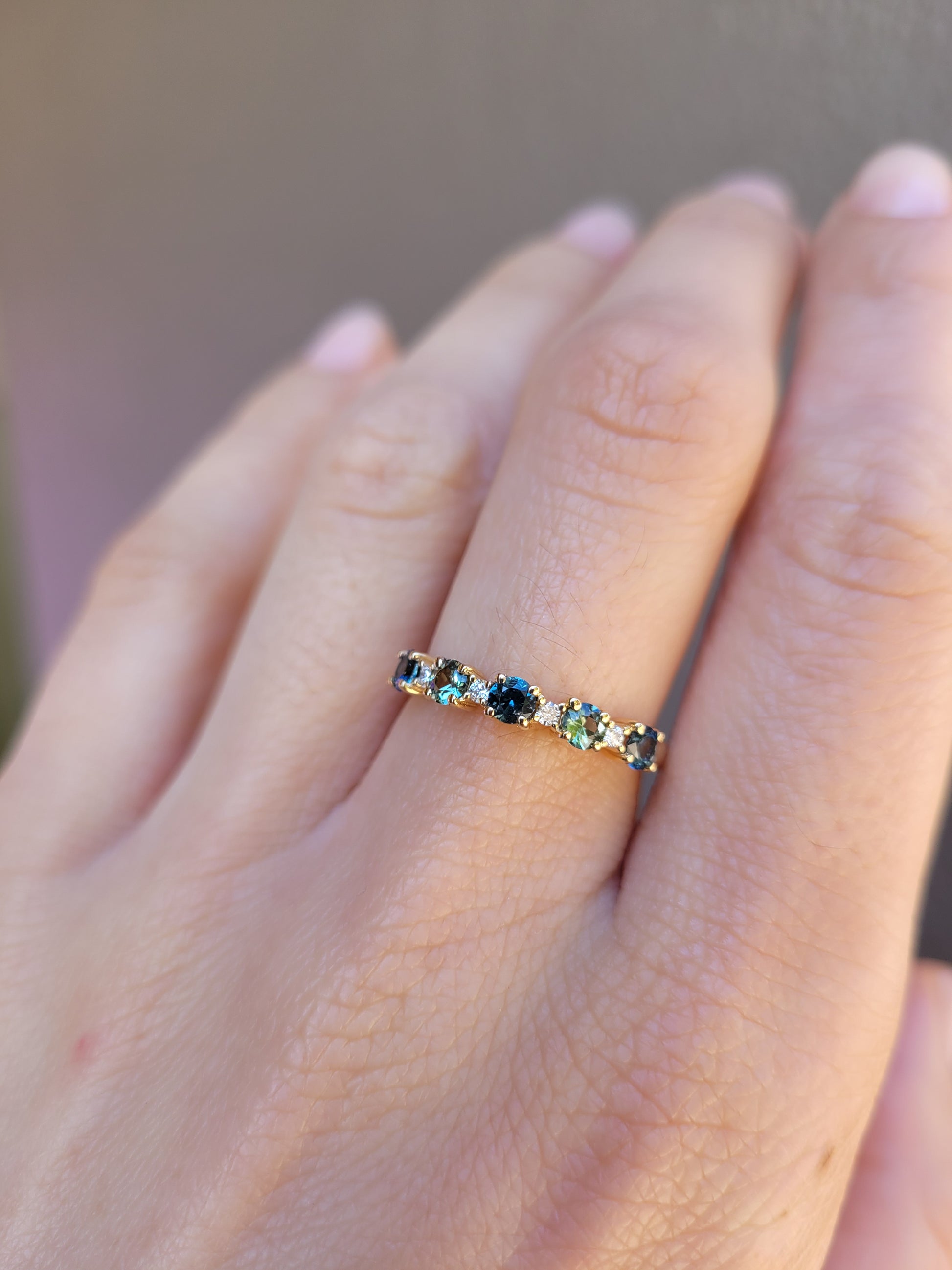 A close-up of a hand wearing a delicate half eternity band ring set with small Australian sapphires and diamonds