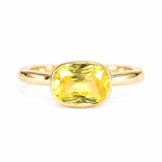 A yellow cushion-cut natural yellow sapphire ring set in a polished yellow gold band, shown against a plain white background.