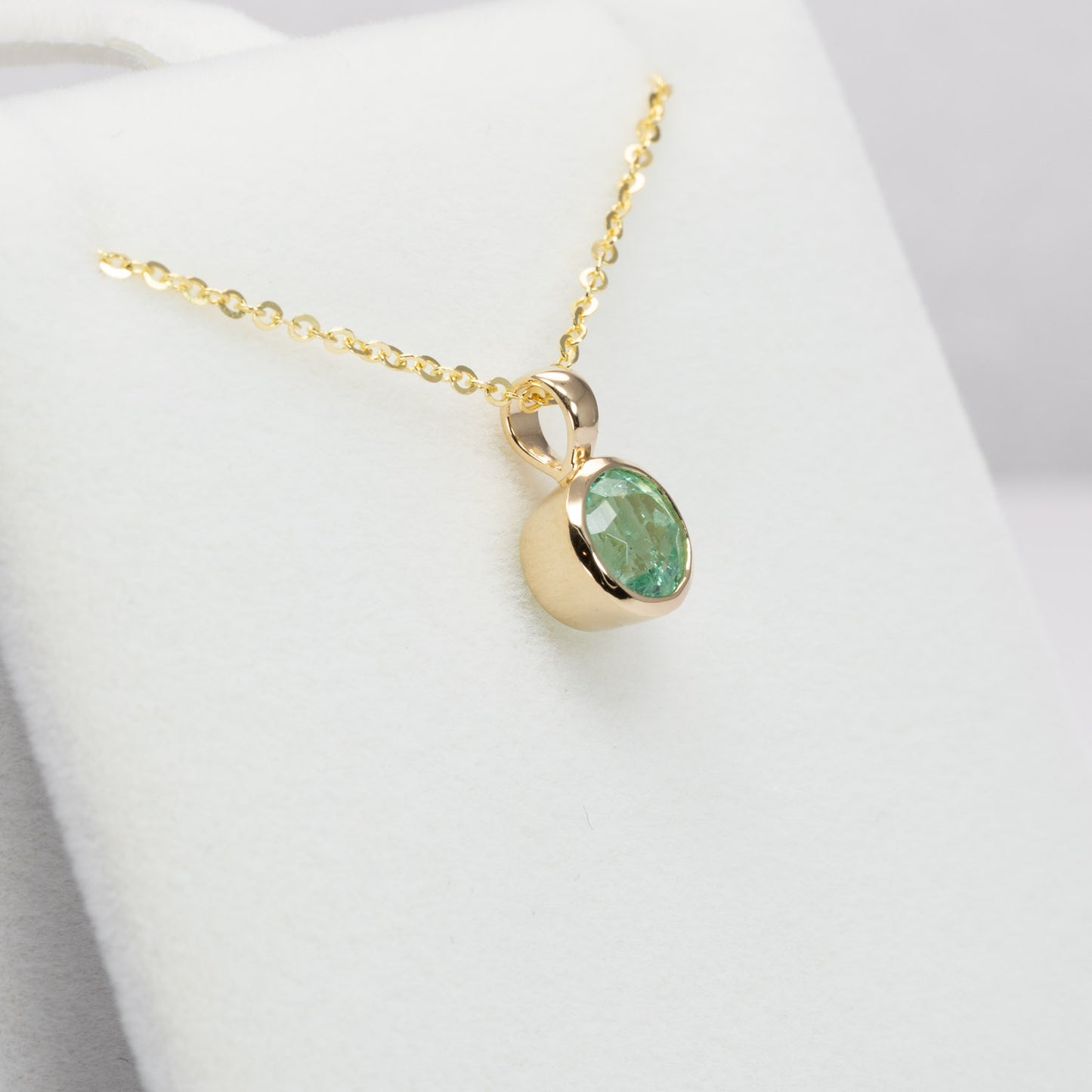 side view of Colombian Emerald Bezel Set Pendant in 18K Yellow Gold with chain in white background