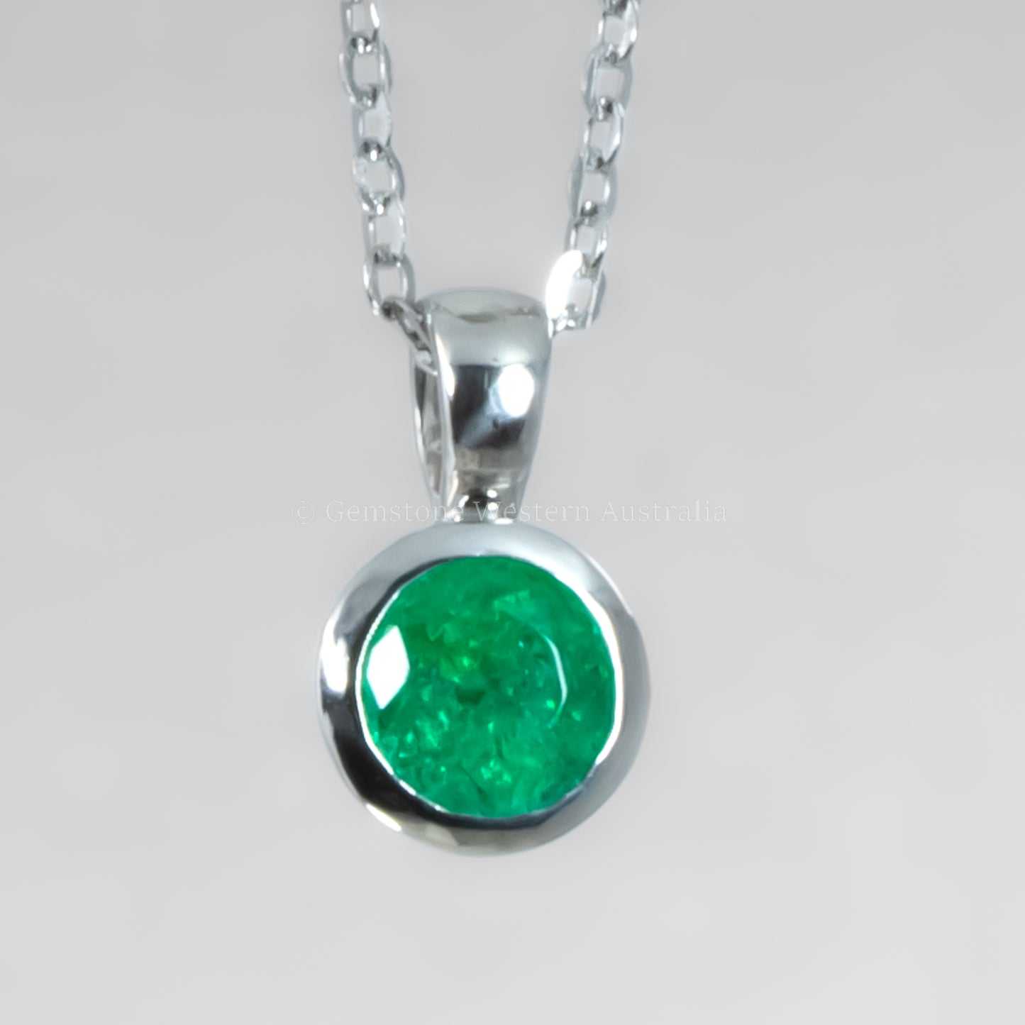 Platinum necklace with an emerald pendant on a light gray background