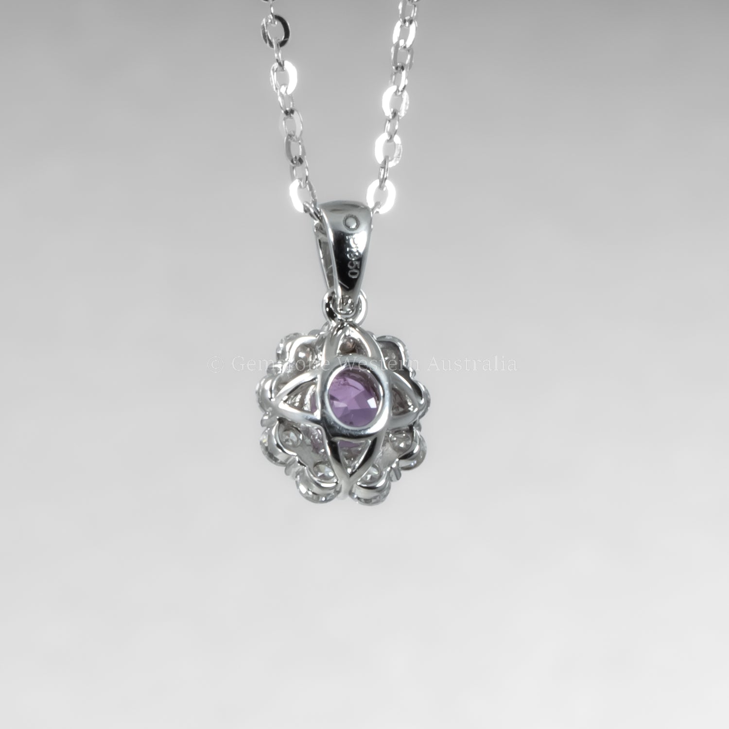 back view of platinum pendant with a pink sapphire on a gray background