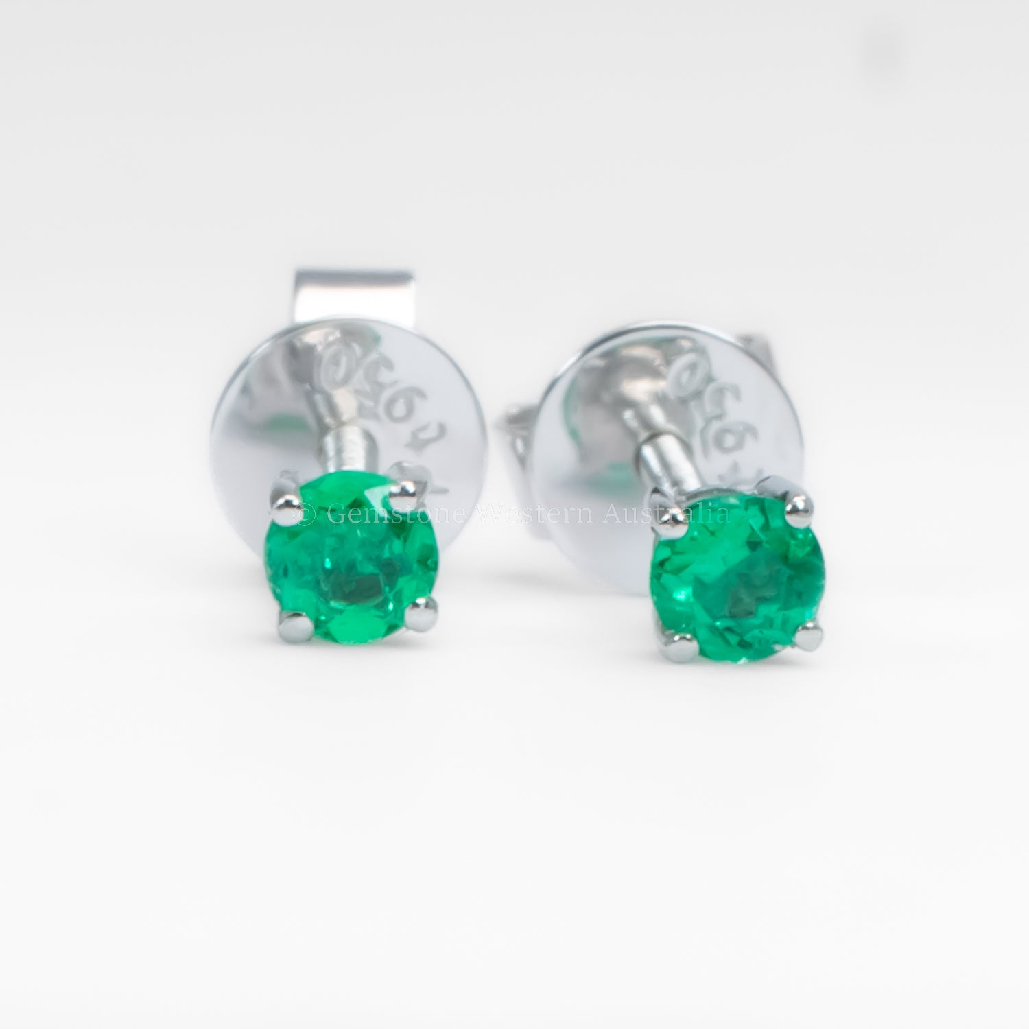 Pair of platinum stud earrings with emerald gemstones on a white background