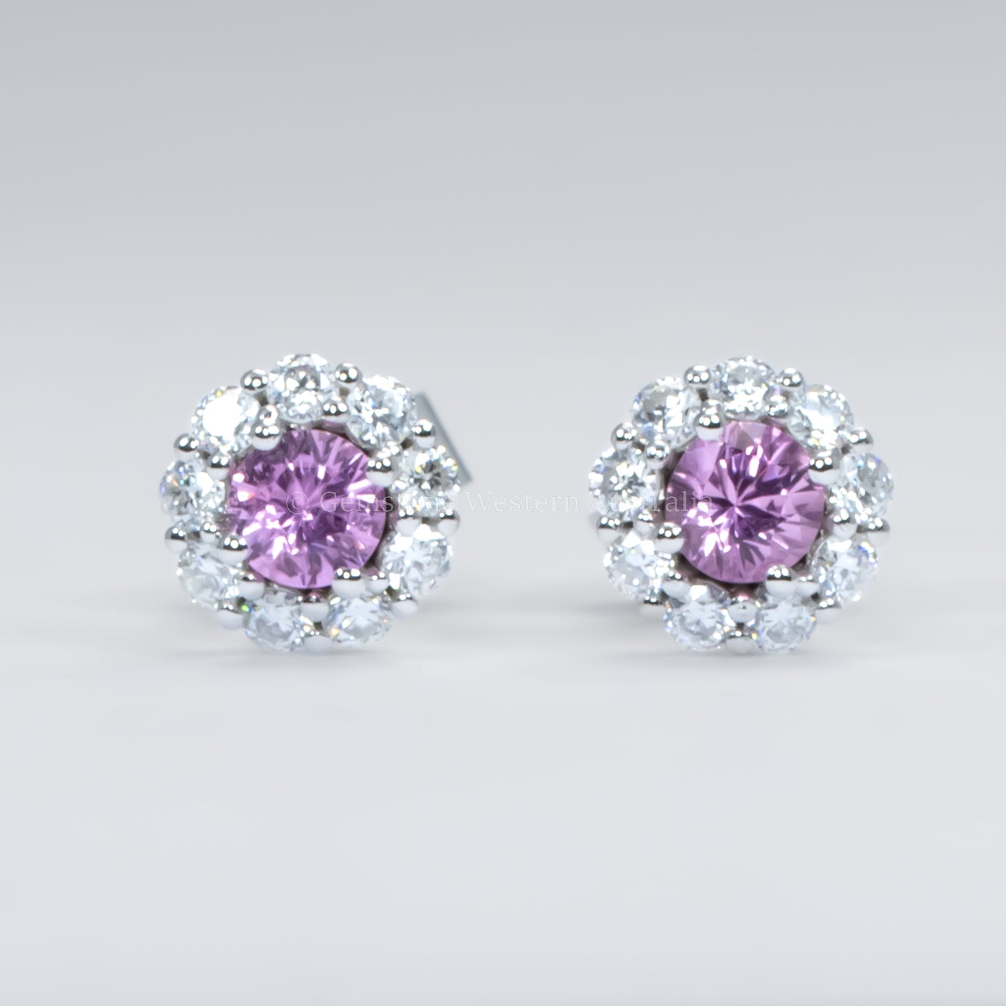 Pair of earrings with pink sapphires and diamond-like stones on a light gray background