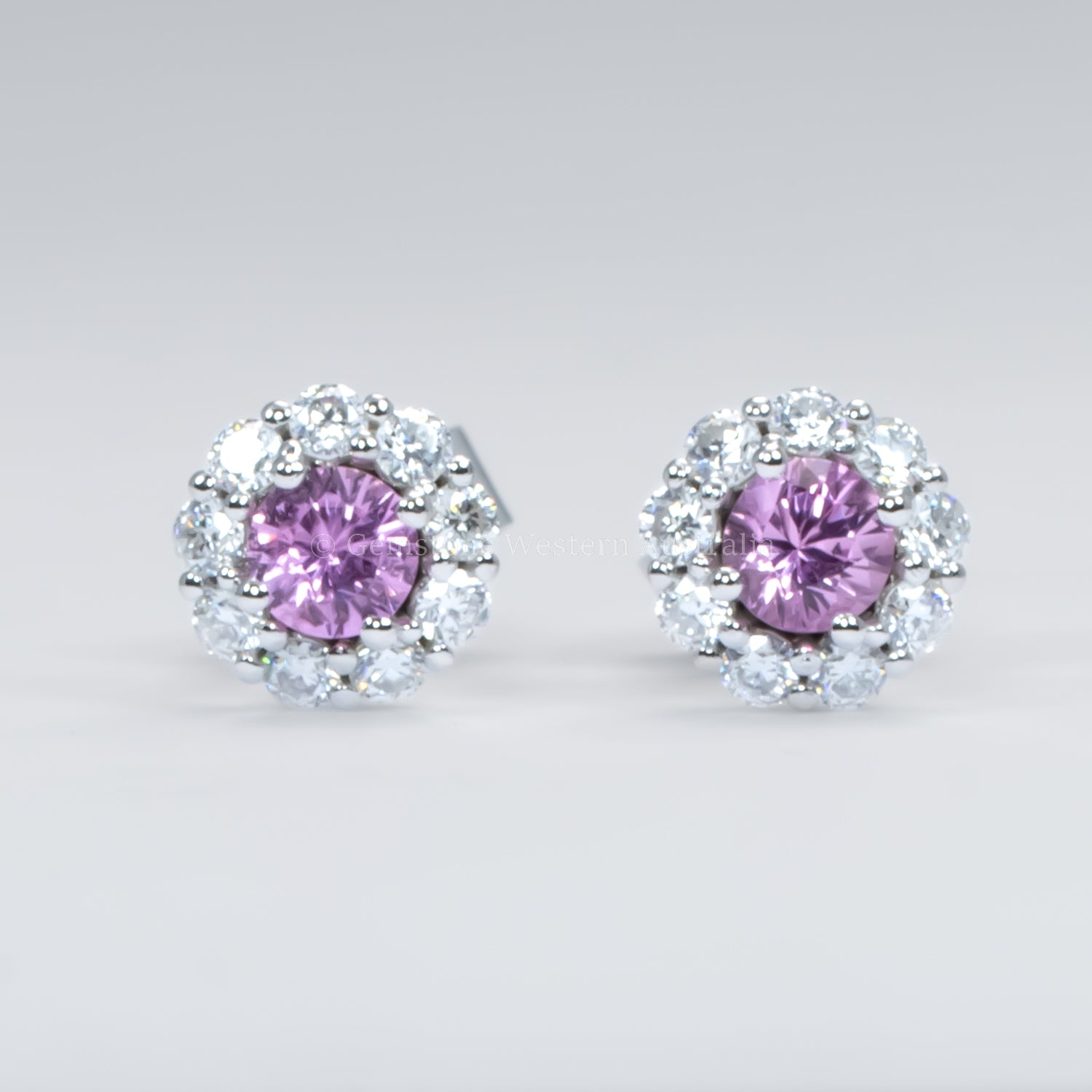 Pair of earrings with pink sapphires and diamond-like stones on a light gray background
