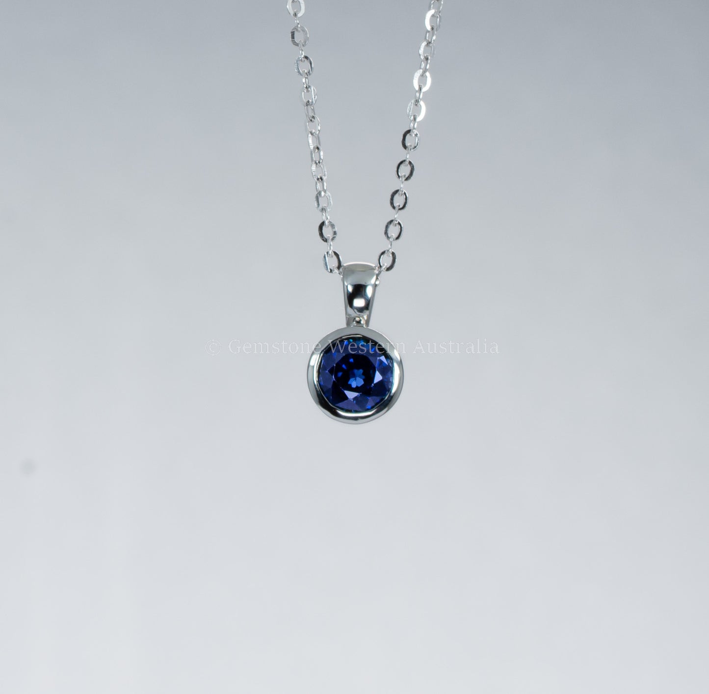 Silver necklace with a blue gemstone pendant on a gray background