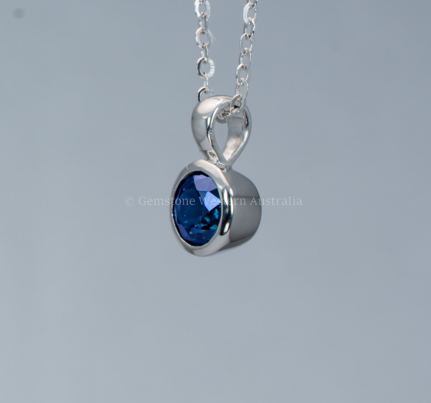 side view platinum pendant with a blue sapphire on a gray background