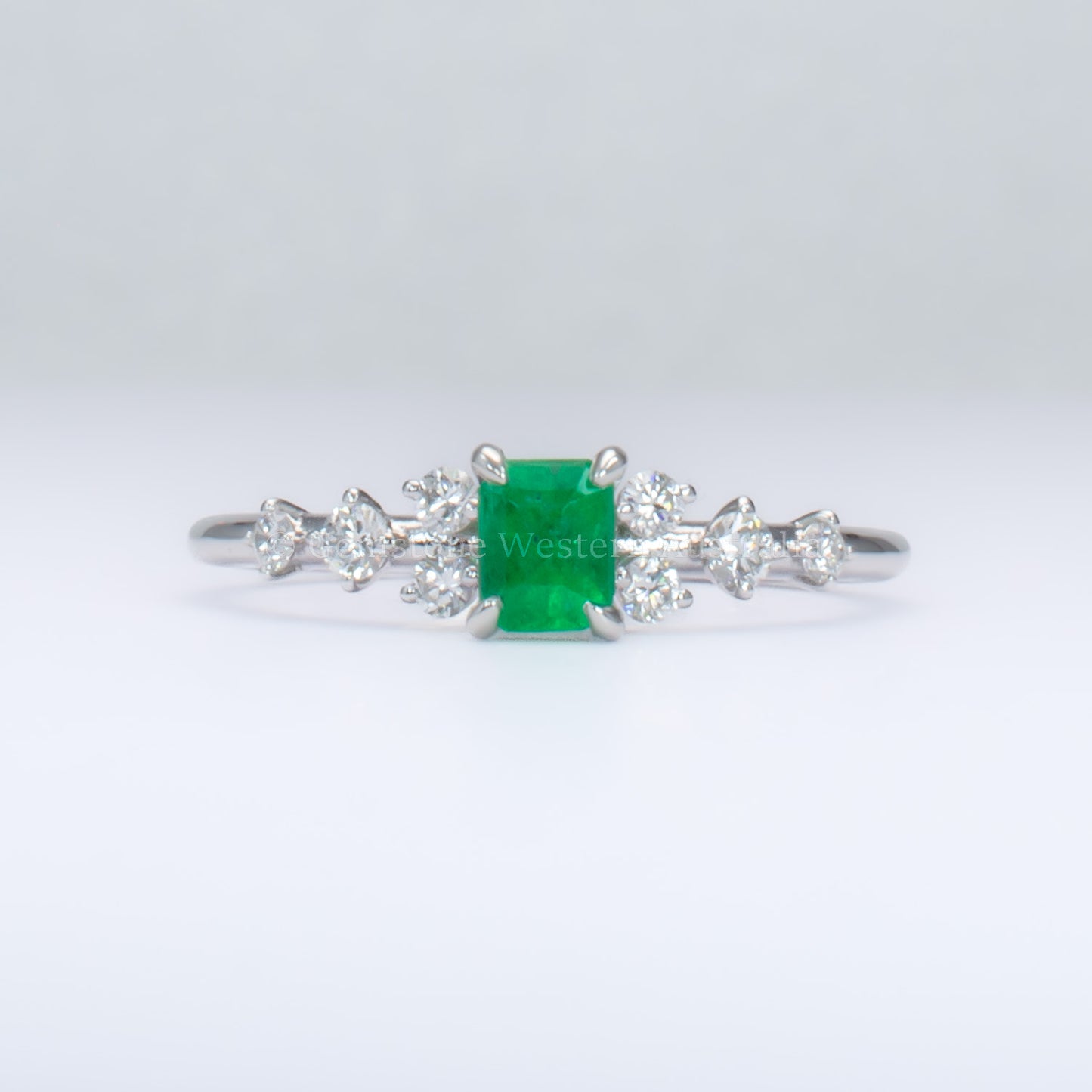 platinum ring with emerald and diamonds in gray background