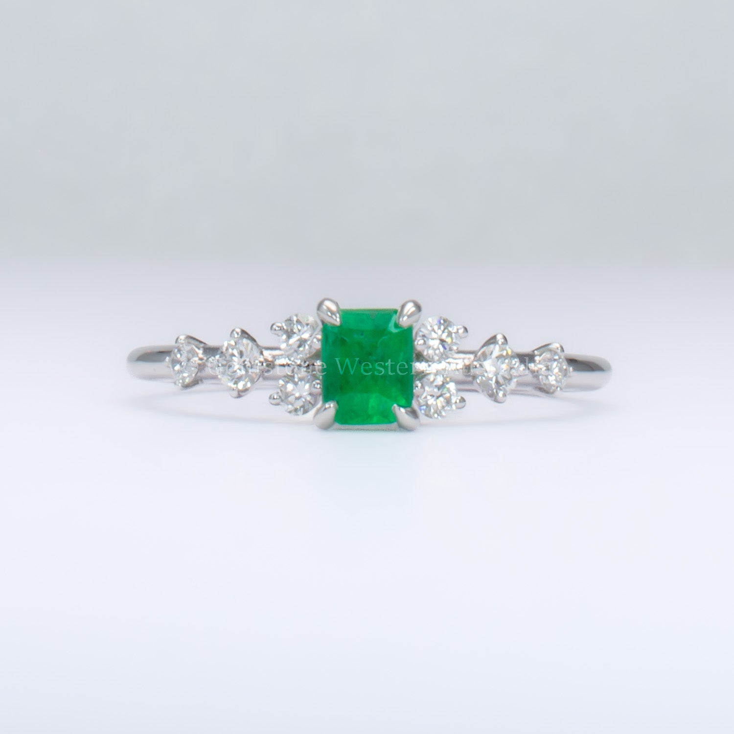 platinum ring with emerald and diamonds in gray background