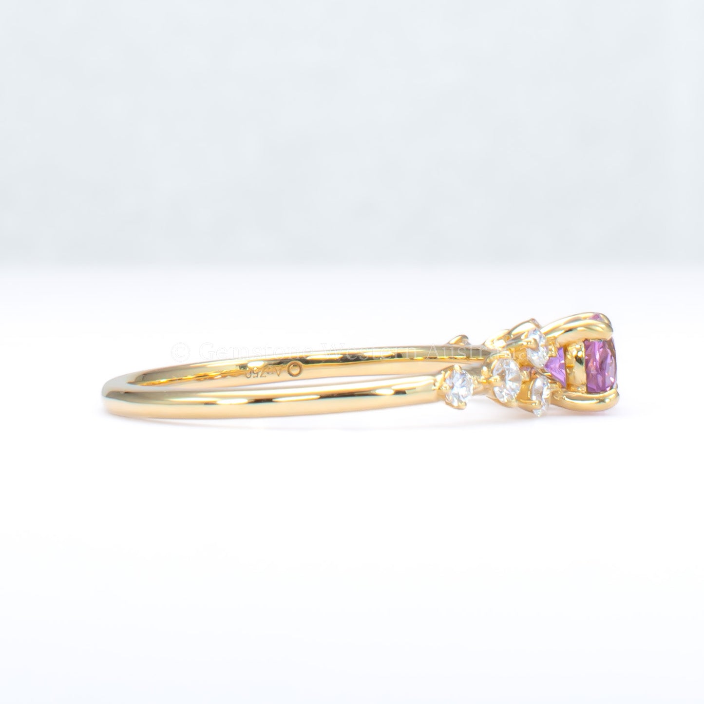 side view of Gold ring with natural pink sapphire and diamonds on a gray background
