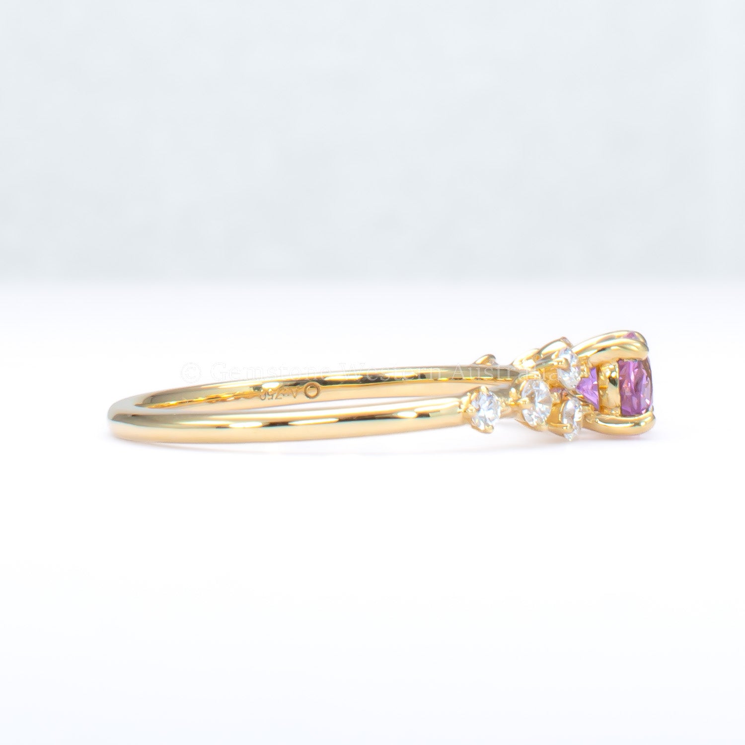 side view of Gold ring with natural pink sapphire and diamonds on a gray background