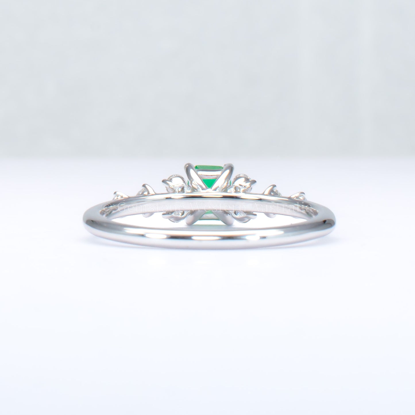 back view of platinum ring with emerald and diamonds in gray background