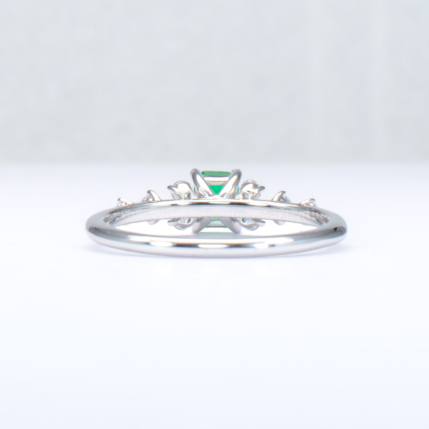back view of platinum ring with emerald and diamonds in gray background