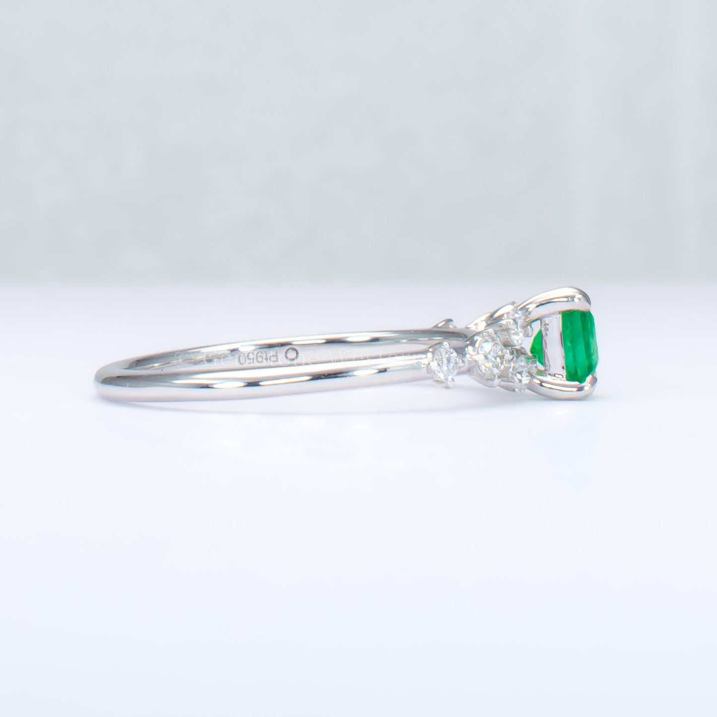 side view of platinum ring with emerald and diamonds in gray background