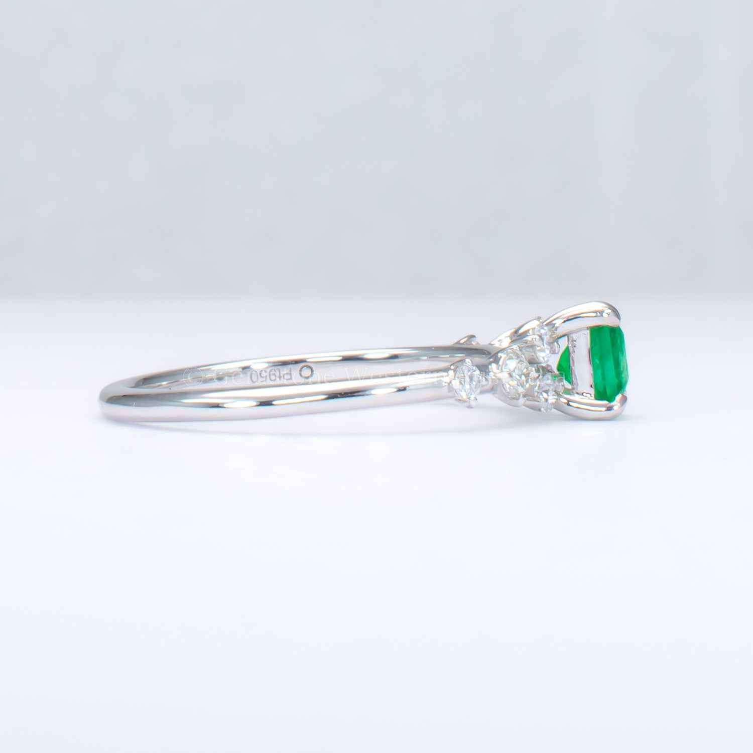side view of platinum ring with emerald and diamonds in gray background