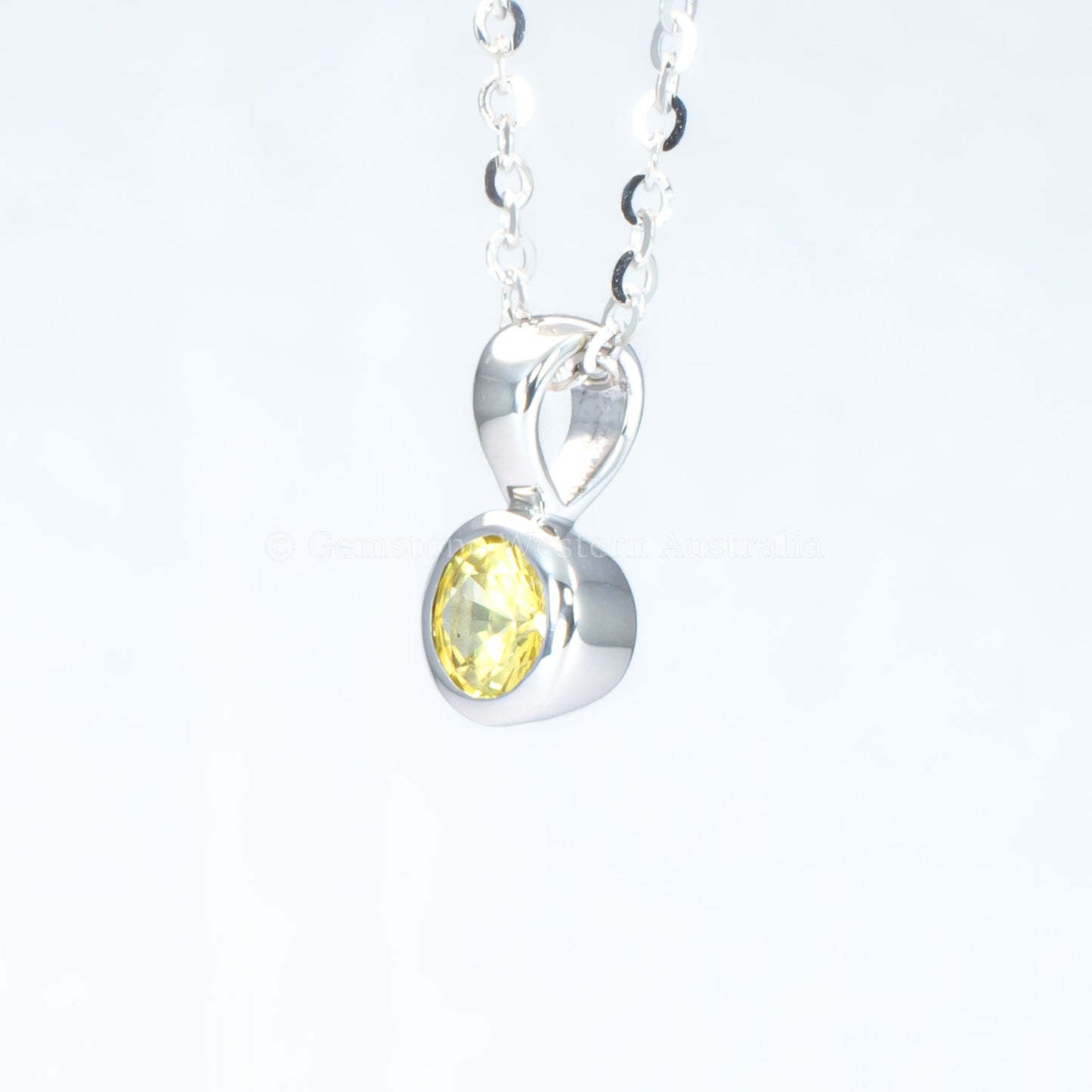 side view of platinum pendant with yellow sapphire in a gray background
