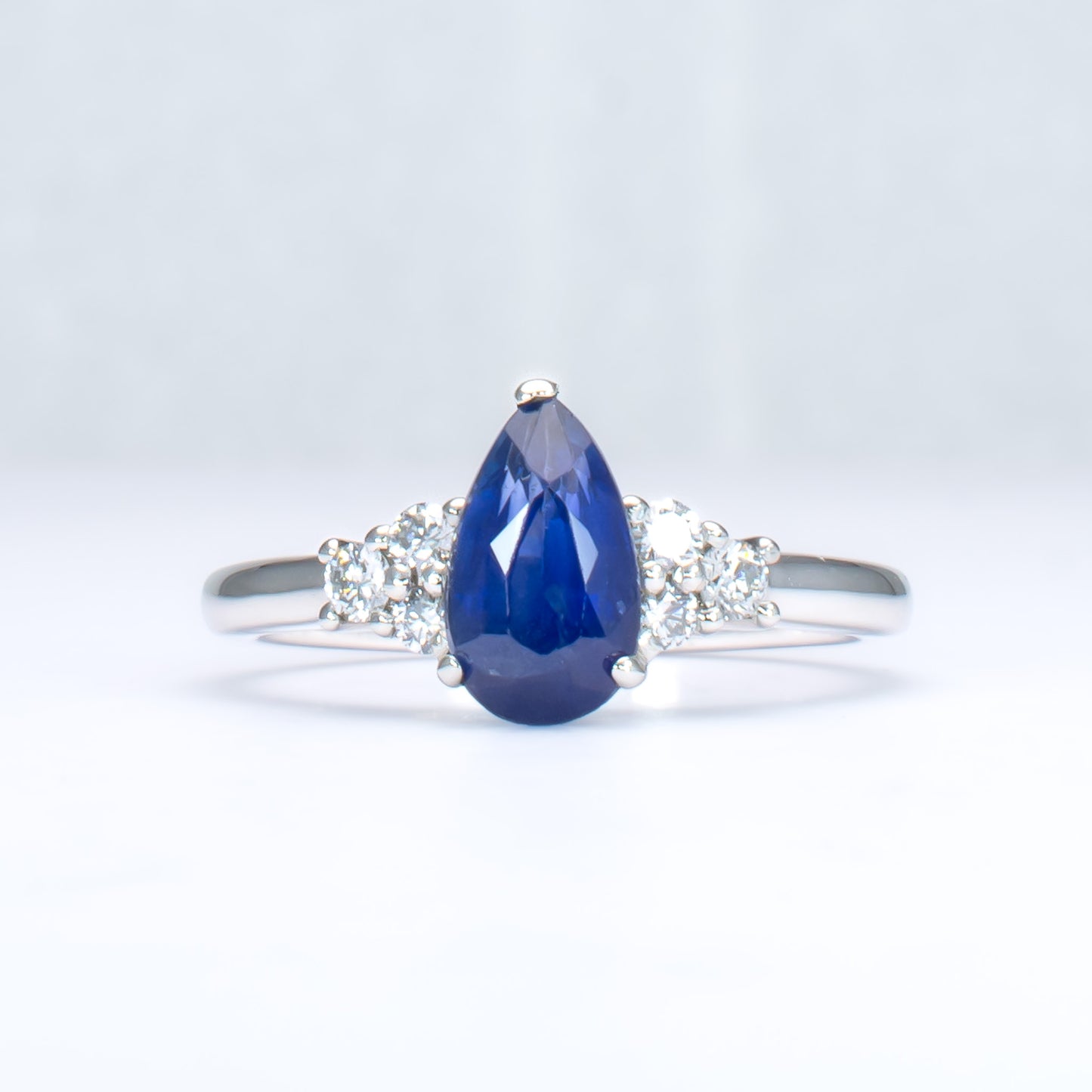 Platinum ring with a blue teardrop-shaped sapphire and smaller diamonds on a light gray background