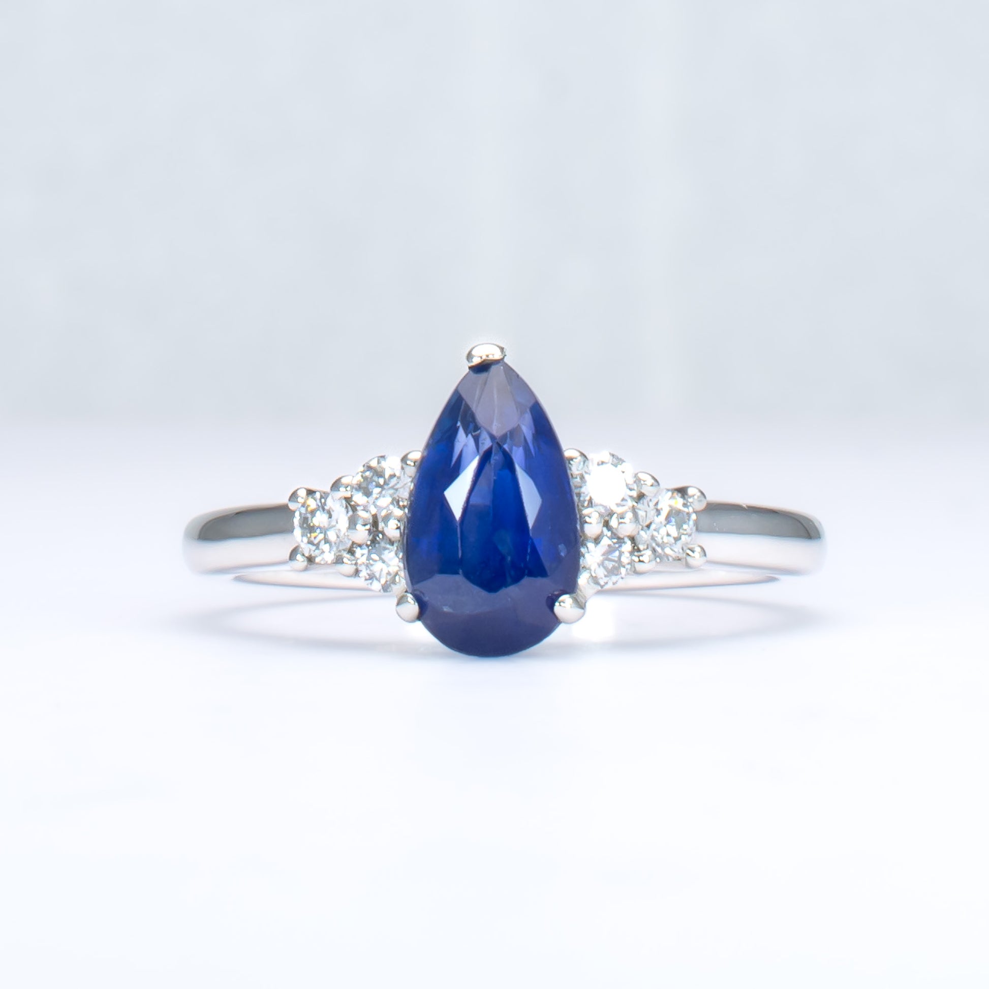 Platinum ring with a blue teardrop-shaped sapphire and smaller diamonds on a light gray background